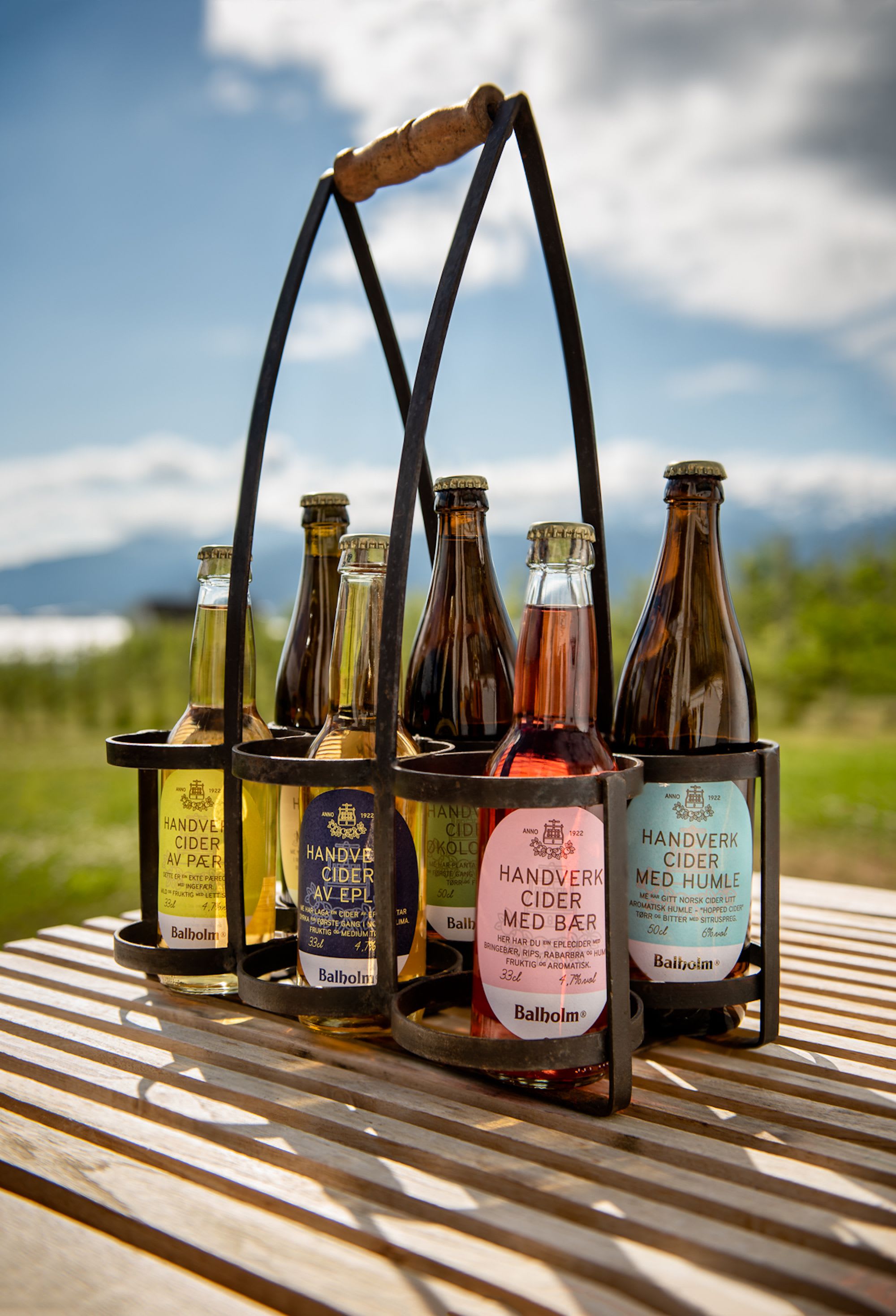Rustic carrier with colorful Balholm cider bottles, inviting a refreshing outdoor tasting experience.