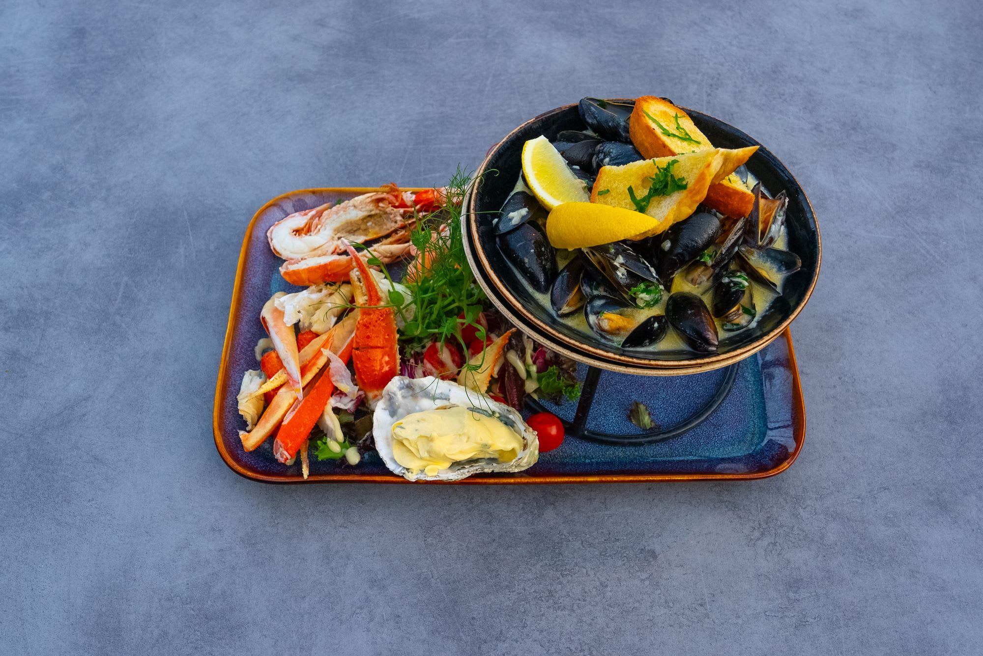 Et sjømatfat servert på en to-etasjes stativ, med blåskjell, krabbe og fargerik sjømat på bunnen.