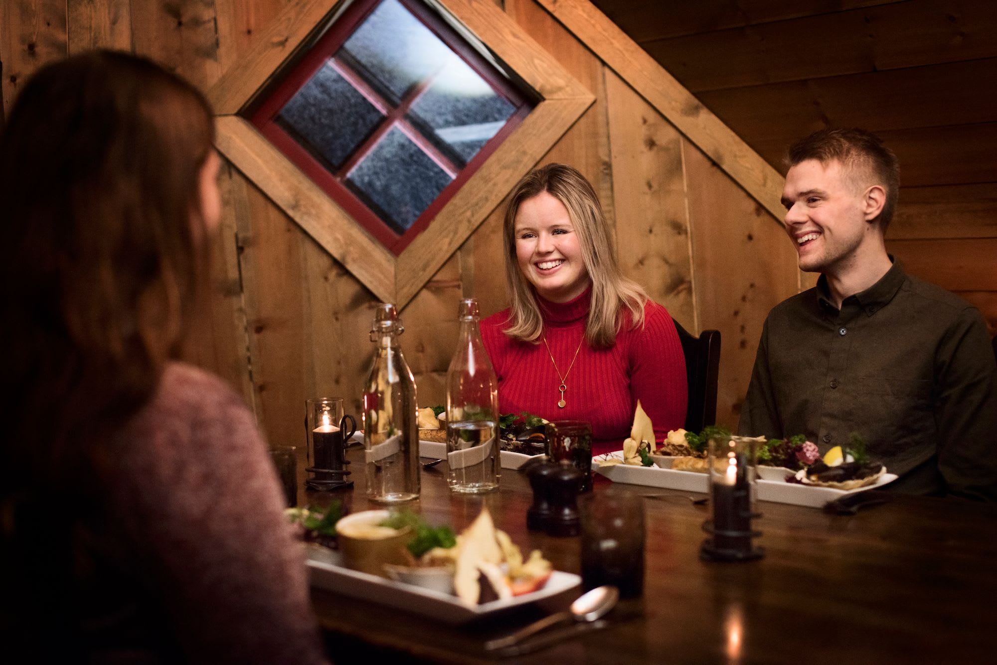 Three friends enjoying a hearty meal at a rustic wooden table in a cozy restaurant, smiling and laughing together.