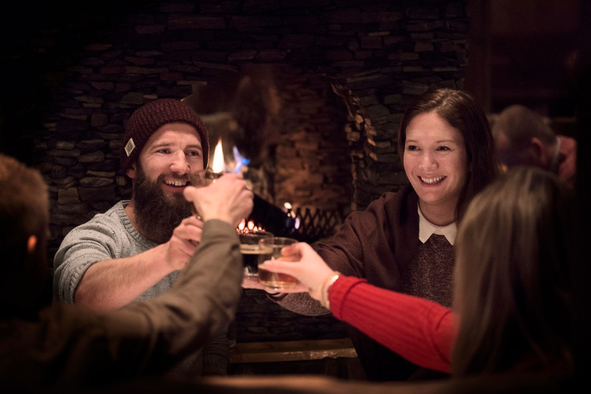 Friends gathered around a cozy stone fireplace, raising glasses in a joyful toast, creating a warm, cheerful atmosphere.