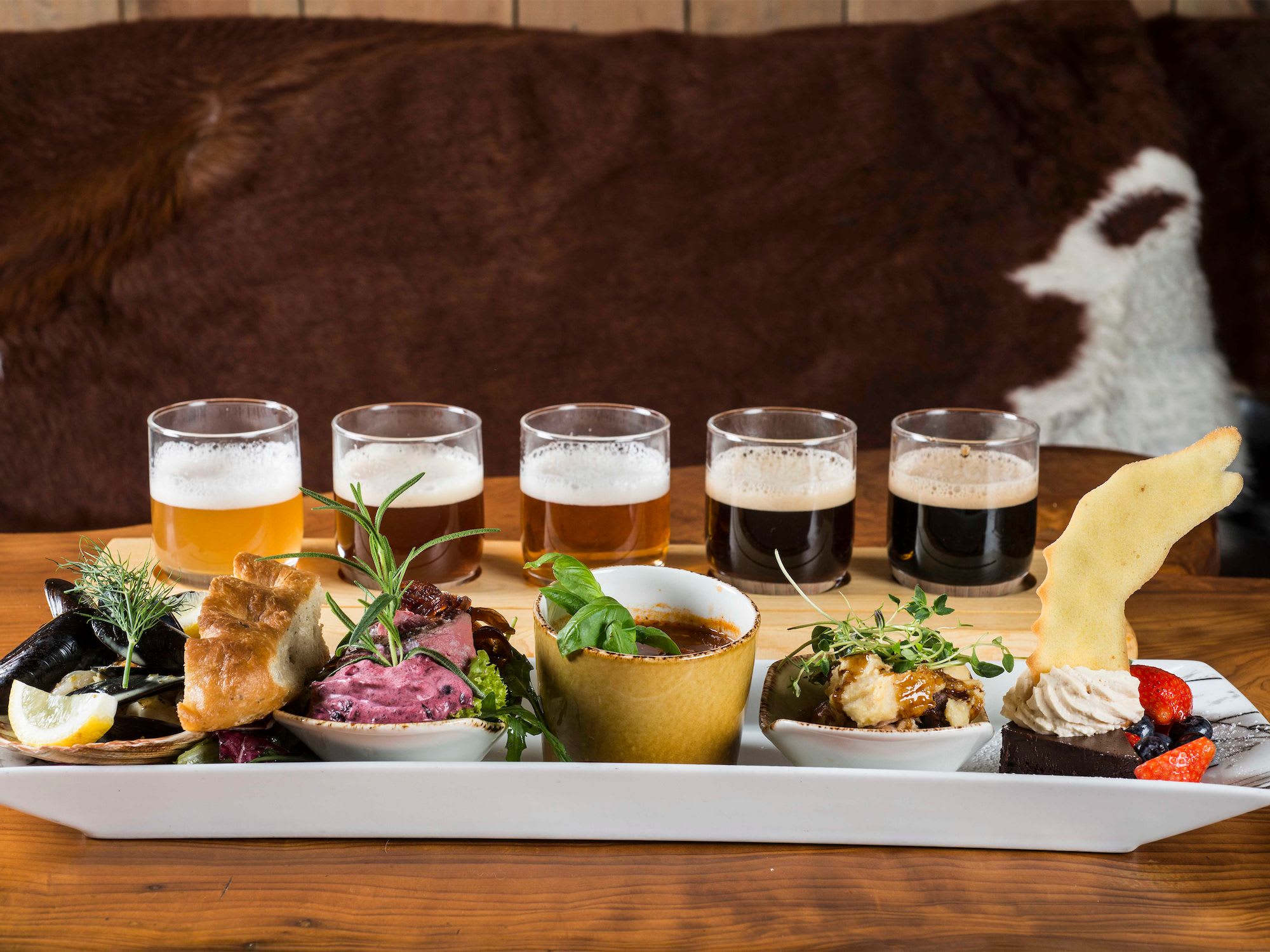 Probierteller mit Muscheln, Brot, Fleisch mit Kräutern, cremigen Gerichten, Schokoladendessert und Craft-Cider in rustikalem Ambiente.