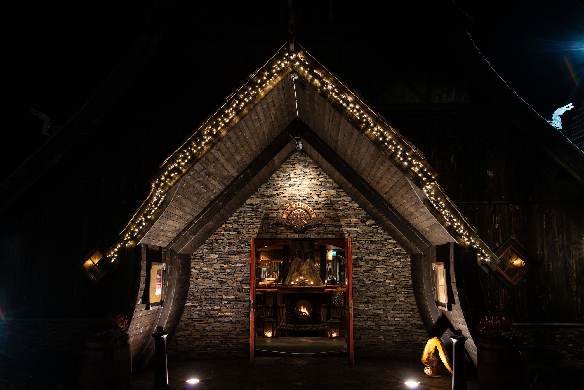 Rustic stone building entrance adorned with fairy lights, cozy interior with fireplace, and whimsical sculpture.