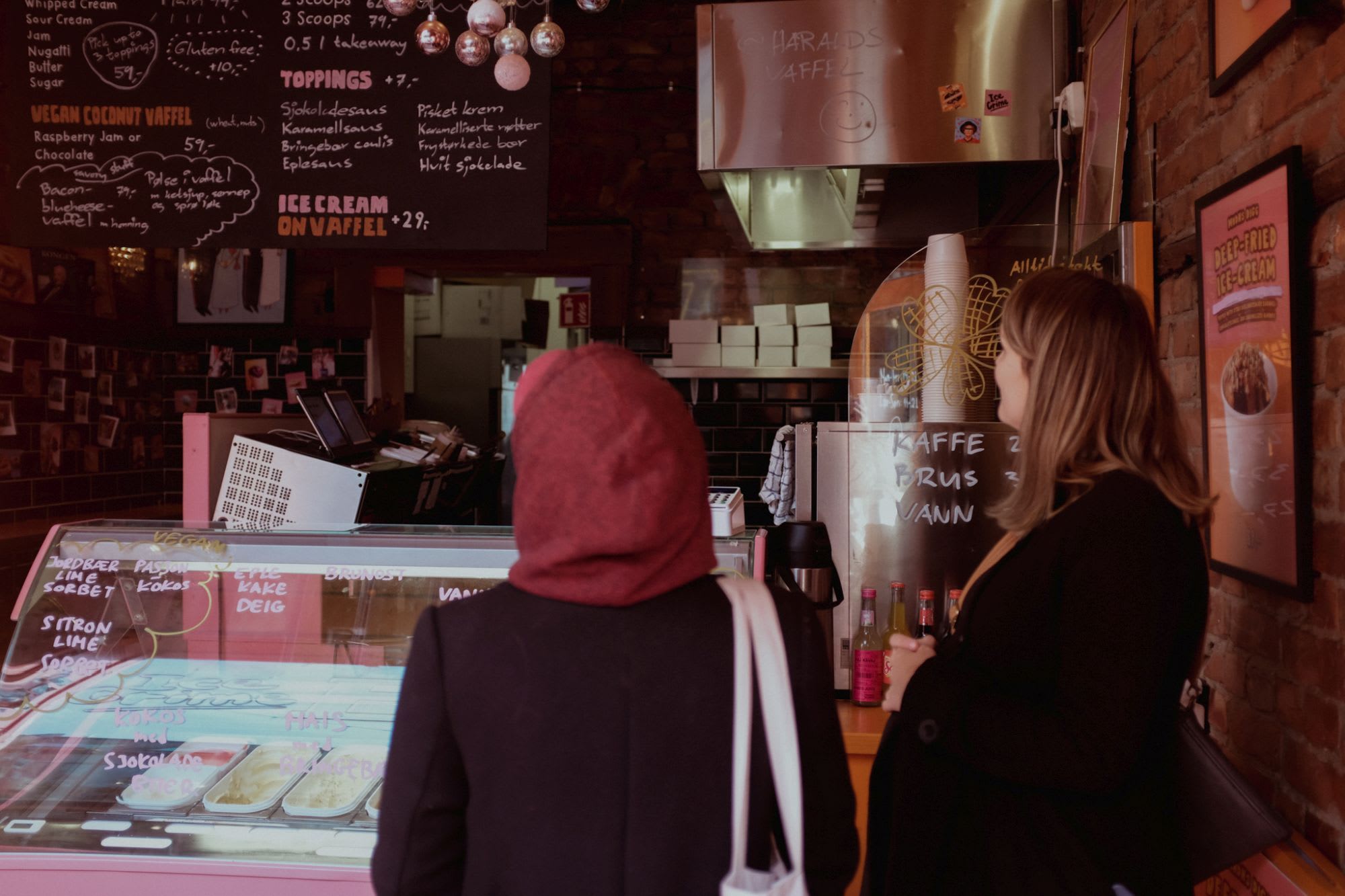 Zwei Frauen lesen das Menü vor einem charmanten Eissalon mit rustikalen Ziegelwänden und gemütlichem, einladendem Innenraum.