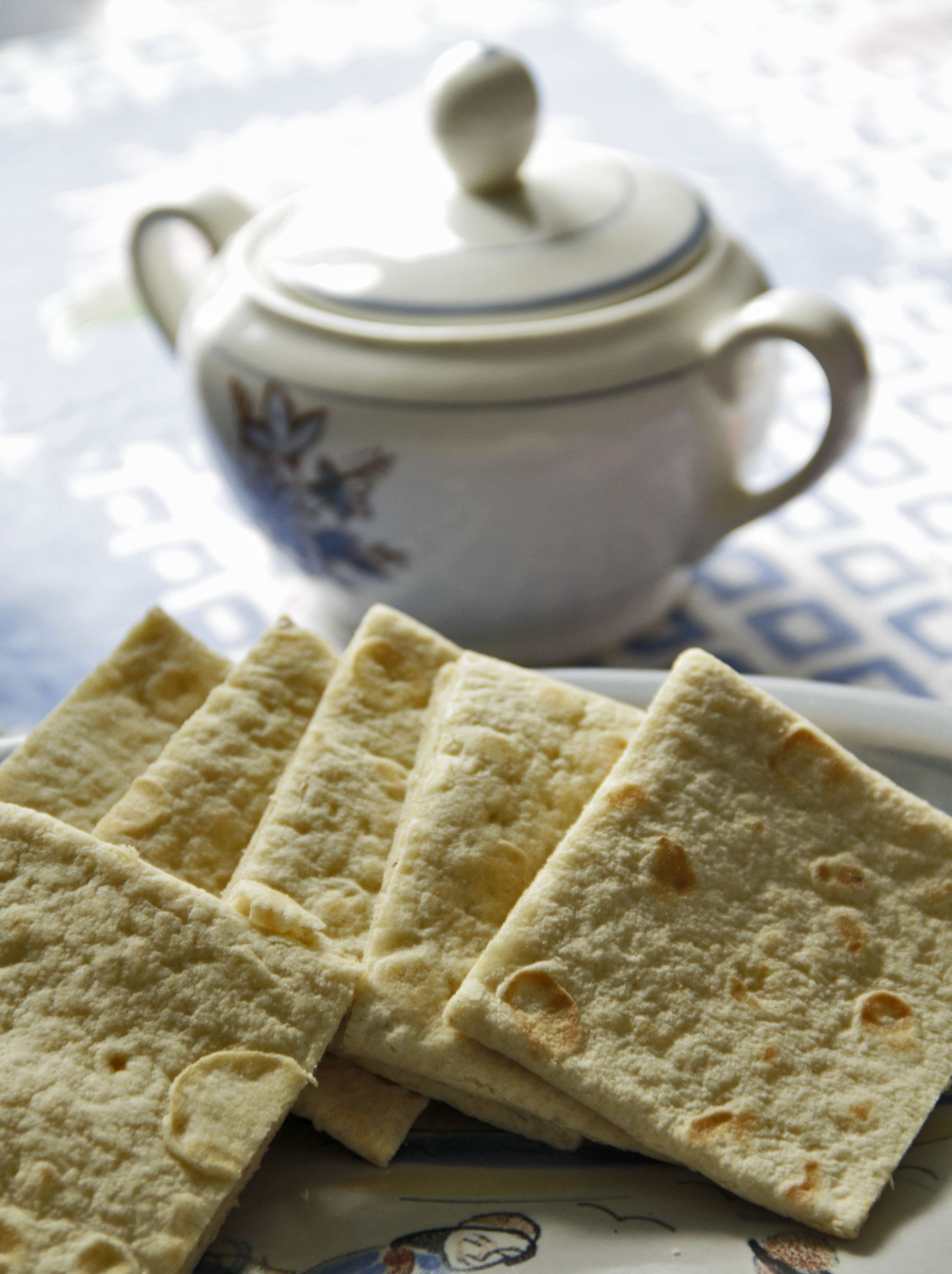 A stack of Flatbrød, a crisp Norwegian bread, arranged neatly on a decorative plate with a ceramic pot nearby.
