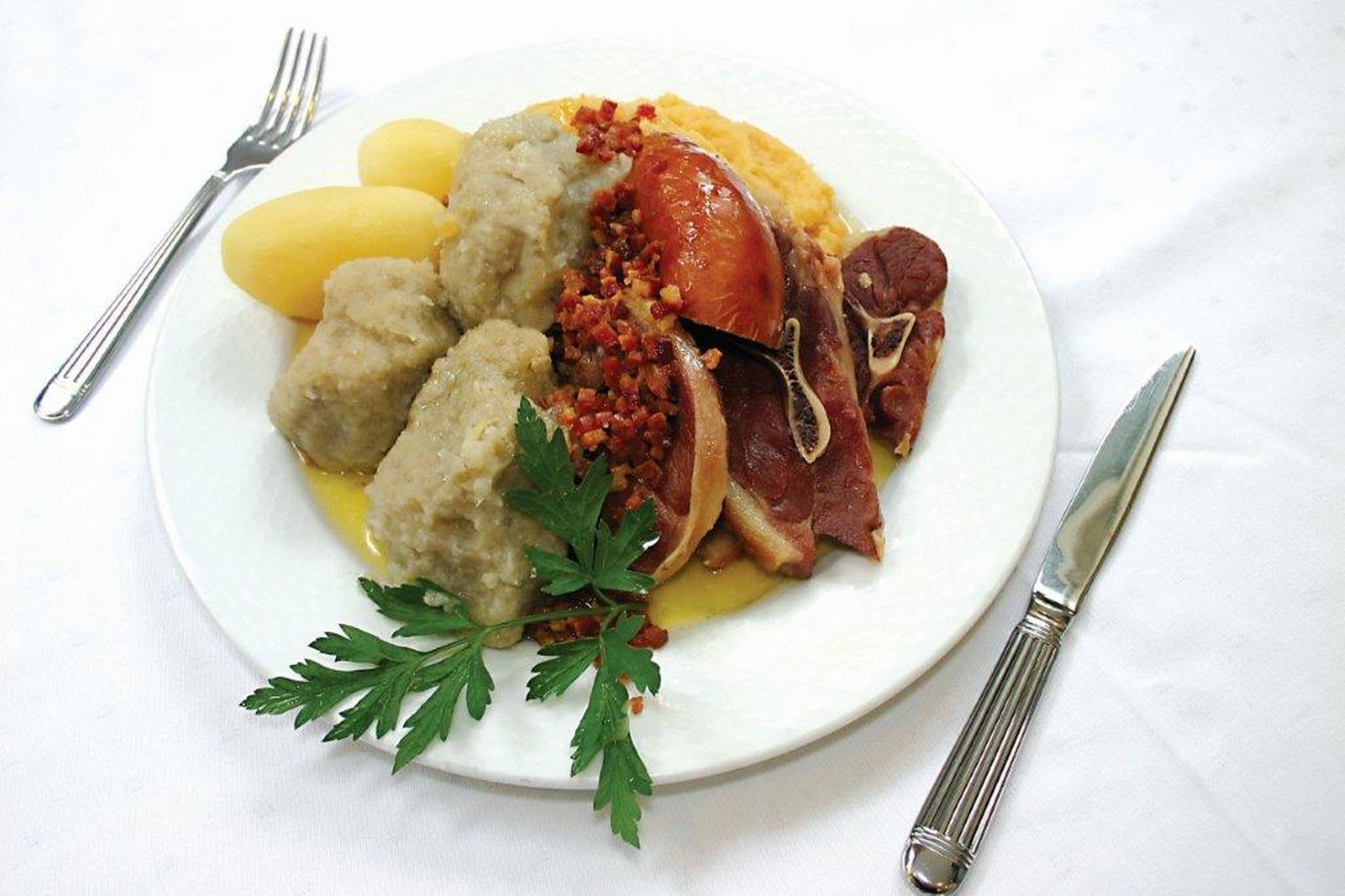 Tradisjonell tallerken med skinke, pølse, bacon, poteter og dumplings i smakfull saus, satt med elegant bestikk.