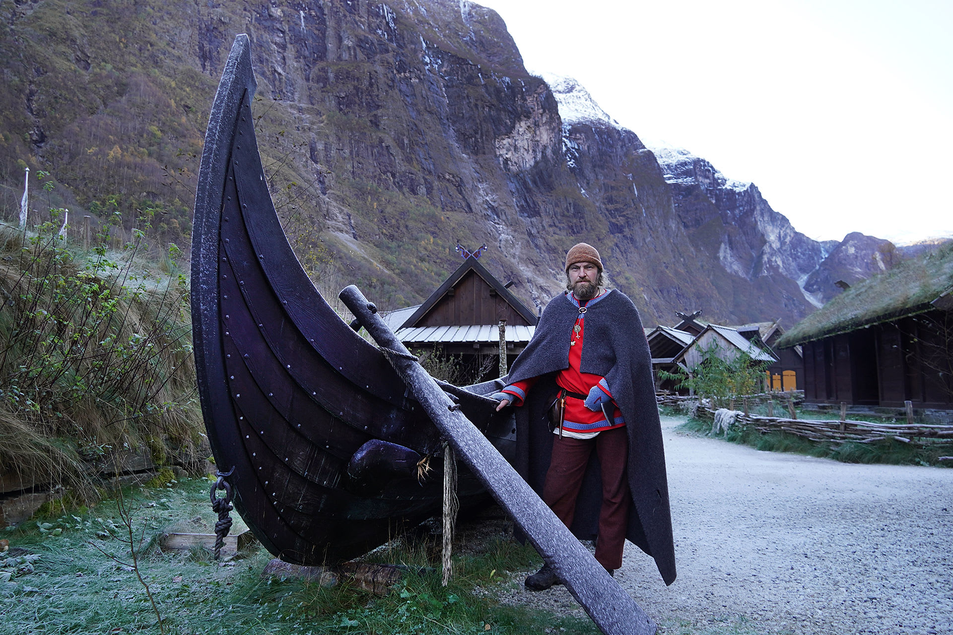 Viking reenactor in traditional Norse clothing at Gudvangen Viking Village with authentic longship and Norwegian mountain backdrop