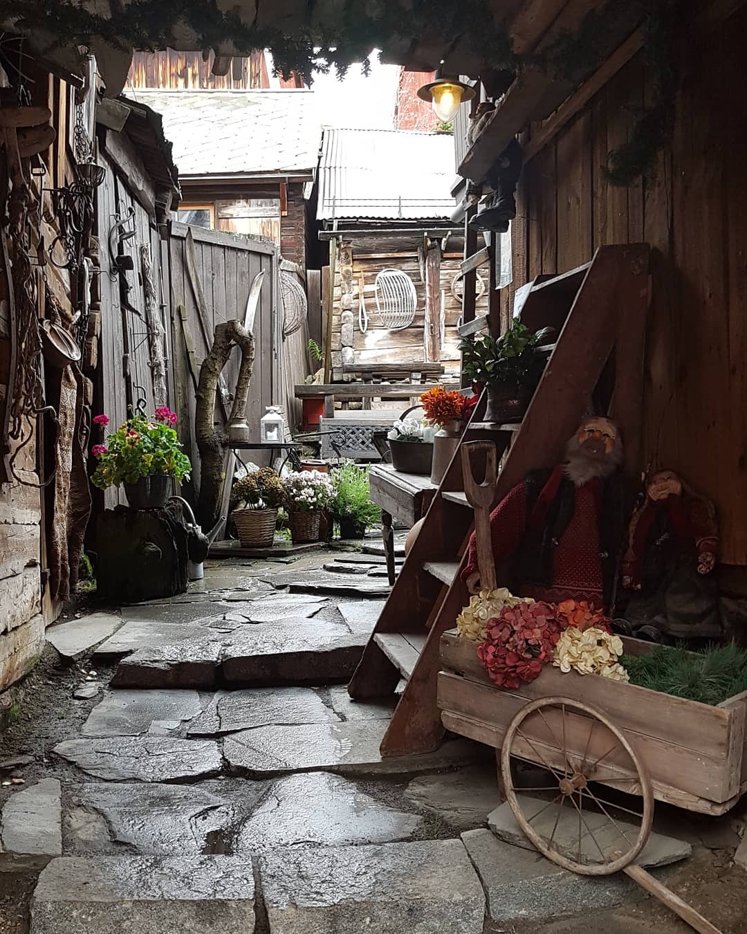 Gemütliche Gasse mit Steinboden, Holz, Blumen und Zwergenfiguren.