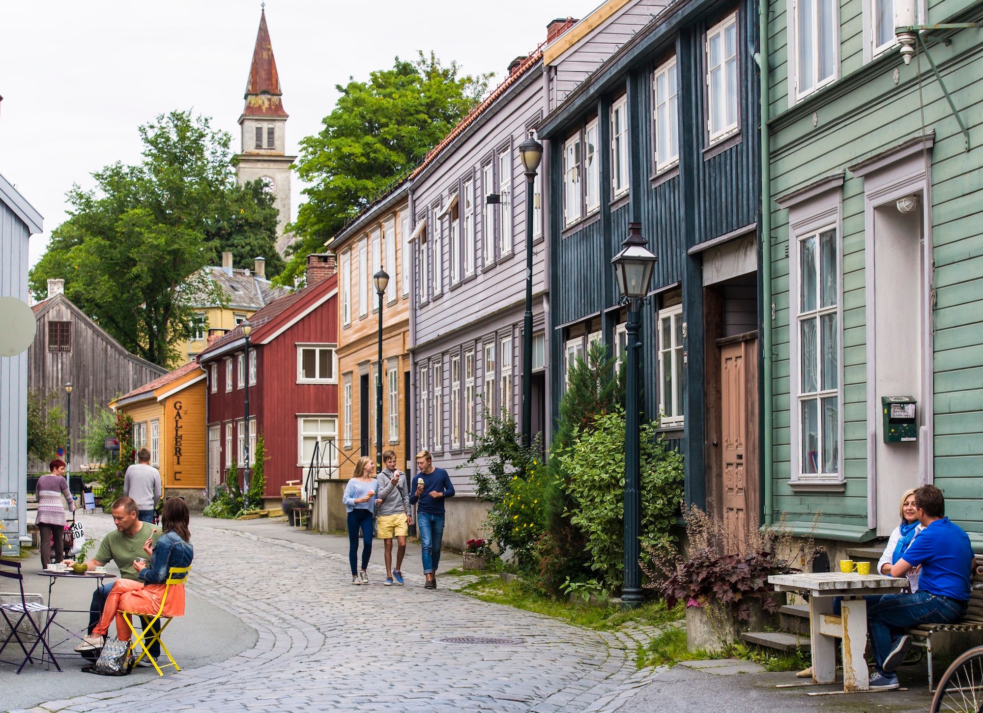 Menschen bummeln und essen an Kopfsteinpflasterstraße mit Kirche.