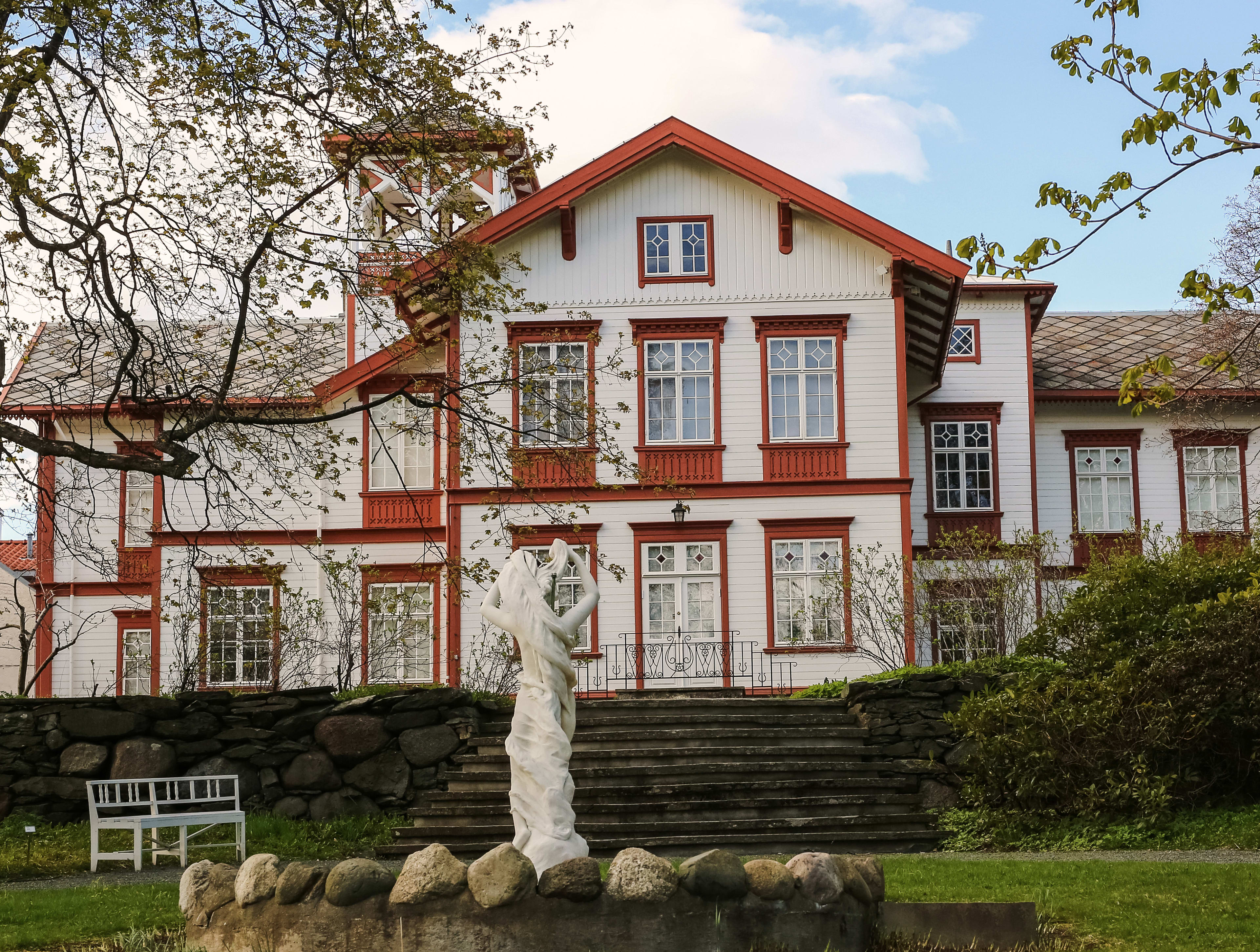 White historic manor building with garden, sculptures and flowering plants at Ringve Museum Trondheim