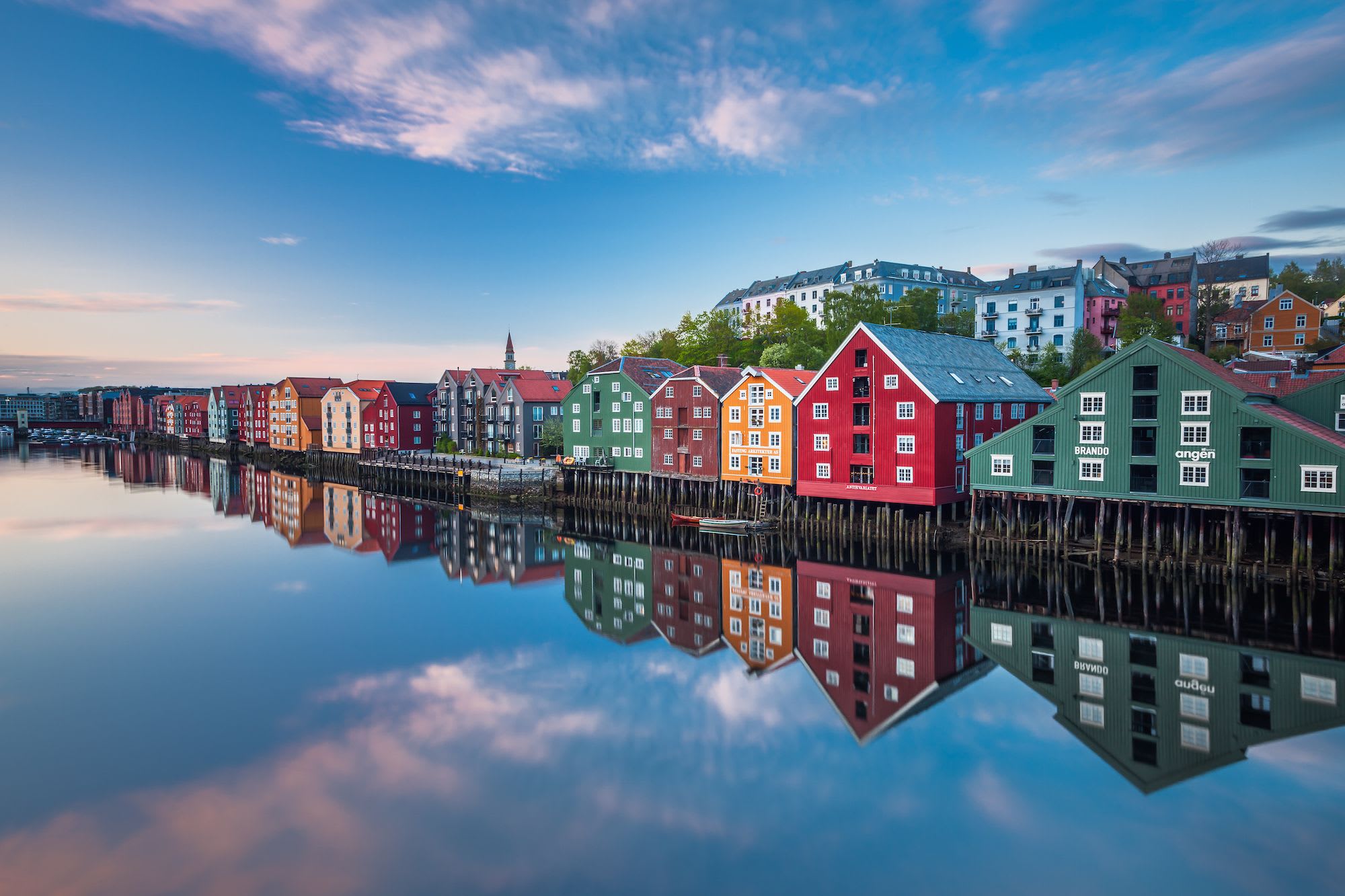 Colorful houses mirrored in still water with soft clouds and hillside behind.