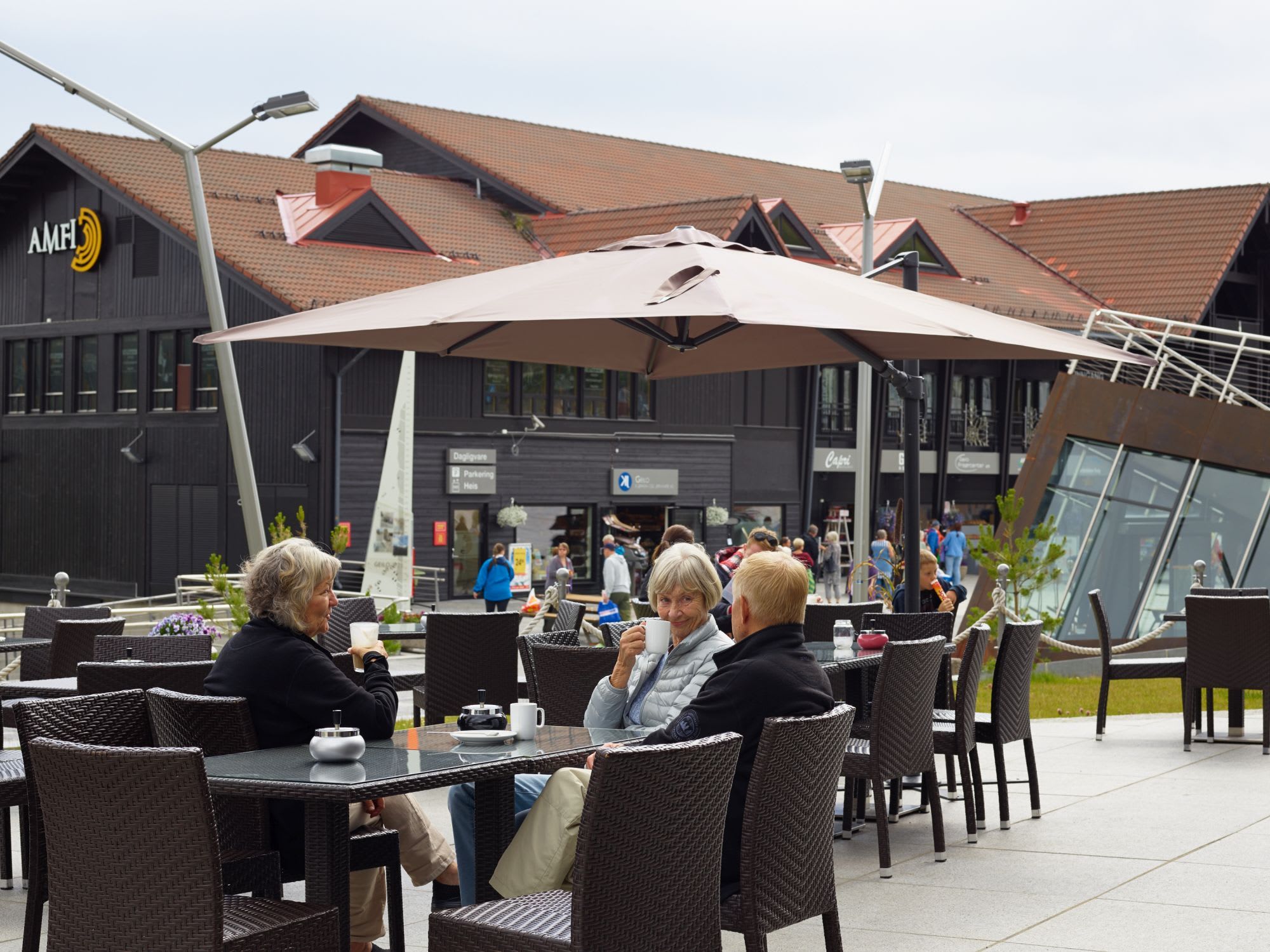 People enjoy drinks at outdoor café near shopping center with wood buildings.