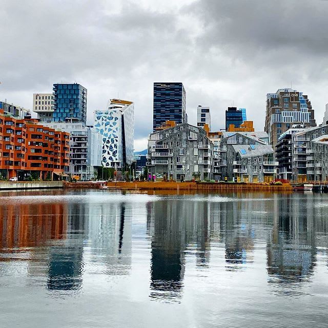 Moderne høyhus speiles i rolig vann under skyet himmel.
