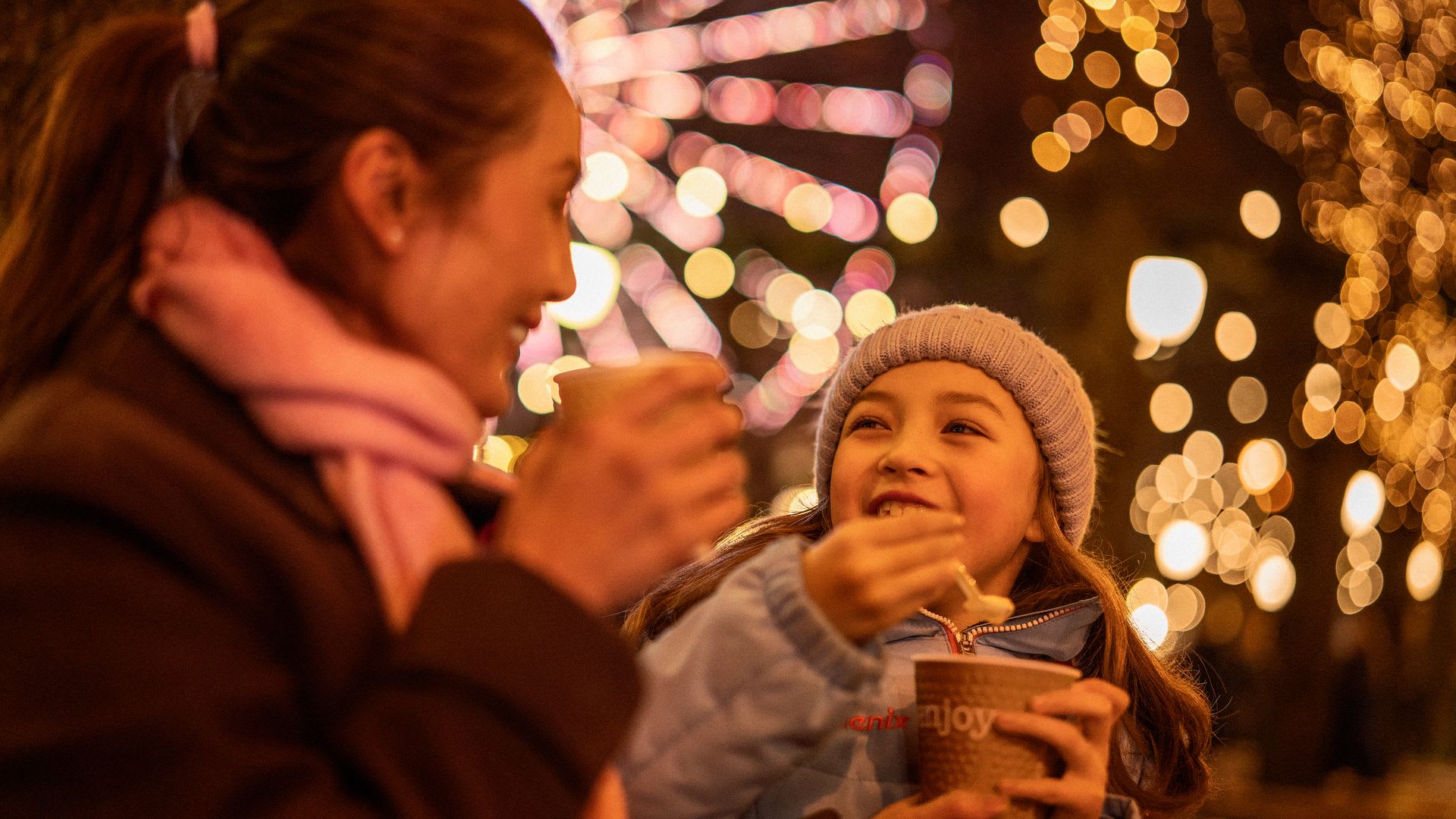 Mor og datter som nyter tradisjonell grøt på Oslos julemarked med festlig belysning