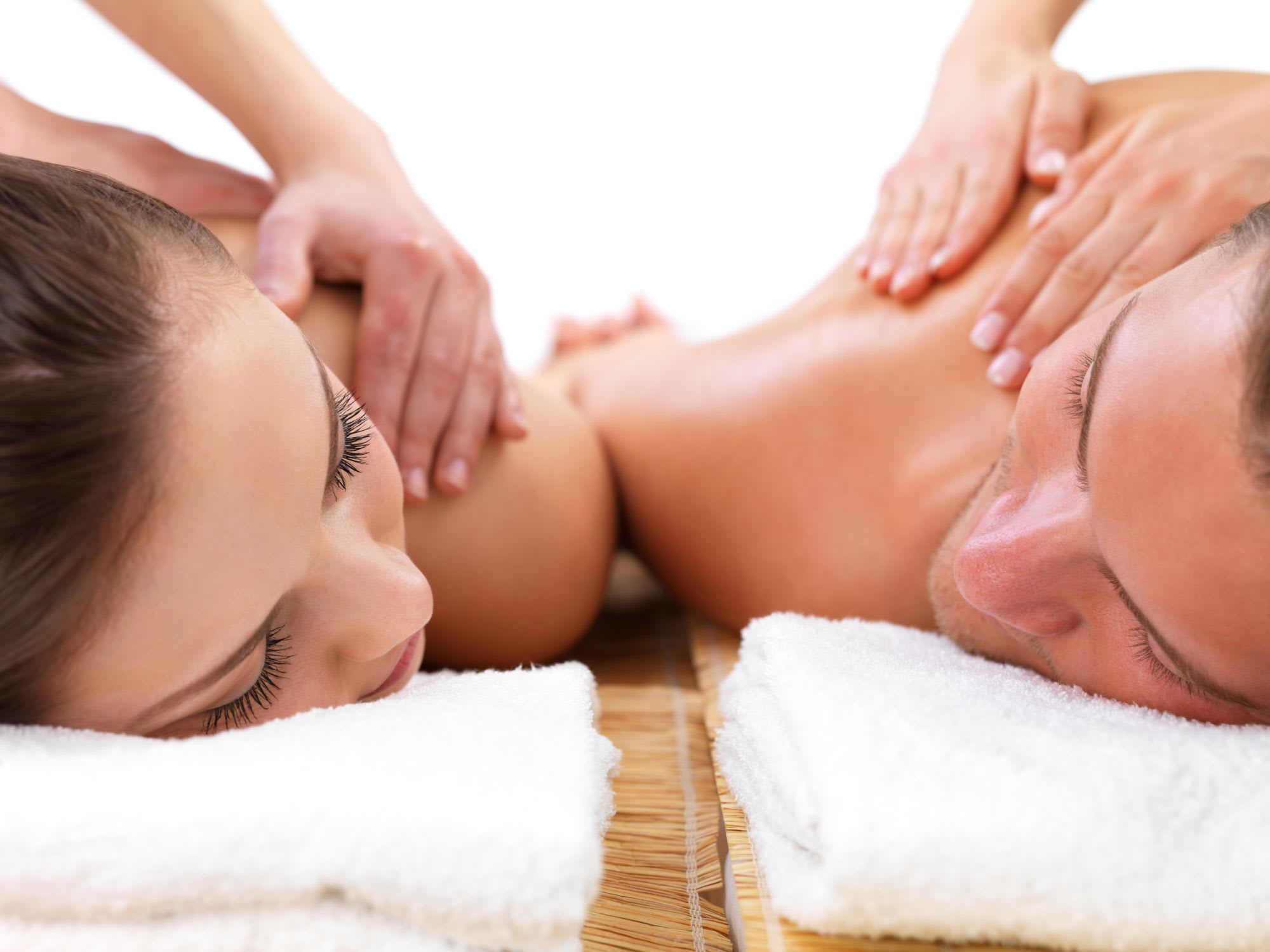 A couple enjoying a massage, lying side-by-side on white towels, eyes closed, relaxed in a serene, soothing atmosphere.