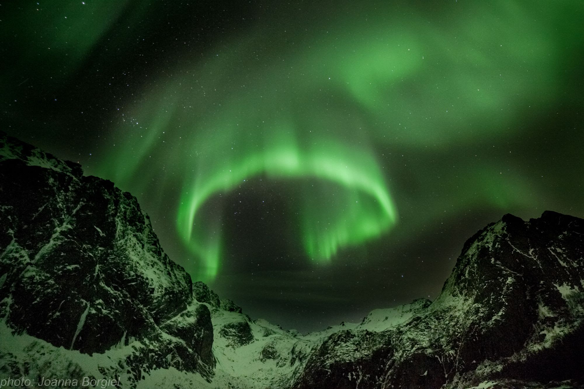 Grønt nordlys danser over snødekte fjell.