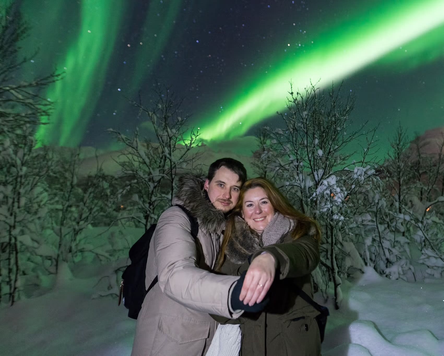 Smilende par poserer sammen med grønne nordlys bak seg