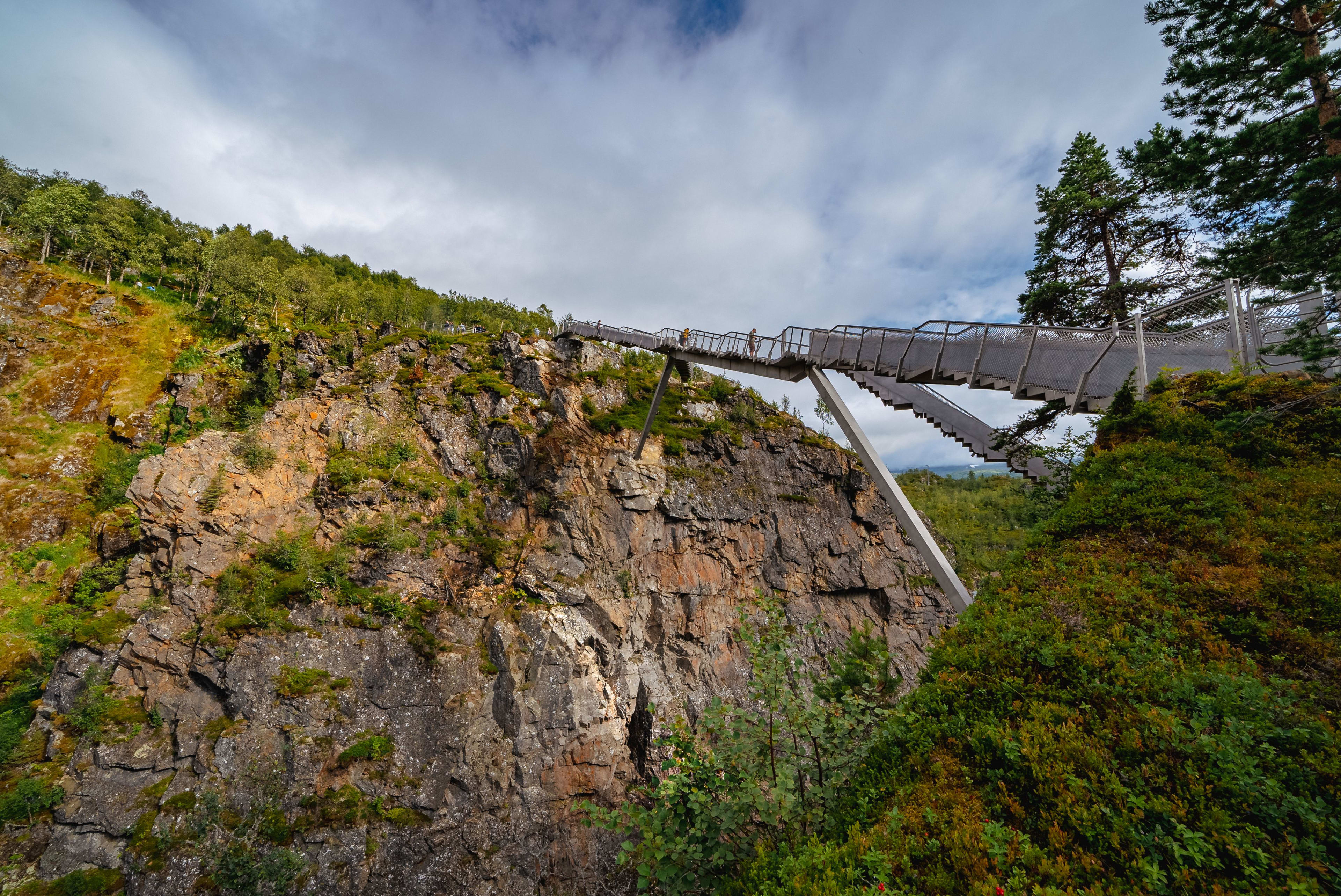 A modern suspension bridge extending across The Vøringsfossen waterfall, offering a stunning view of the landscape with a couple walking.