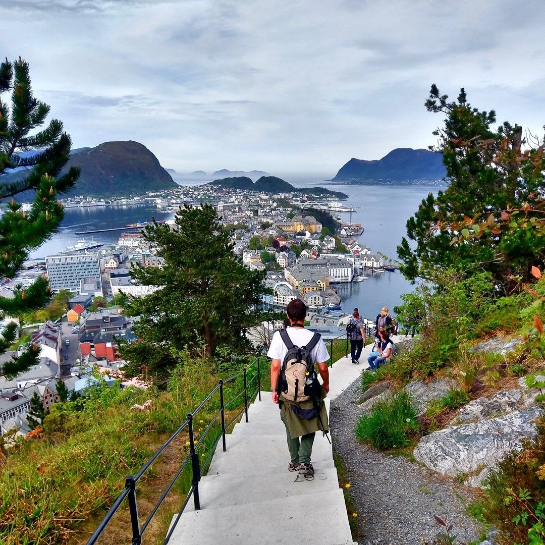 Wanderer auf Treppe mit Blick auf Ålesund und Fjorde.