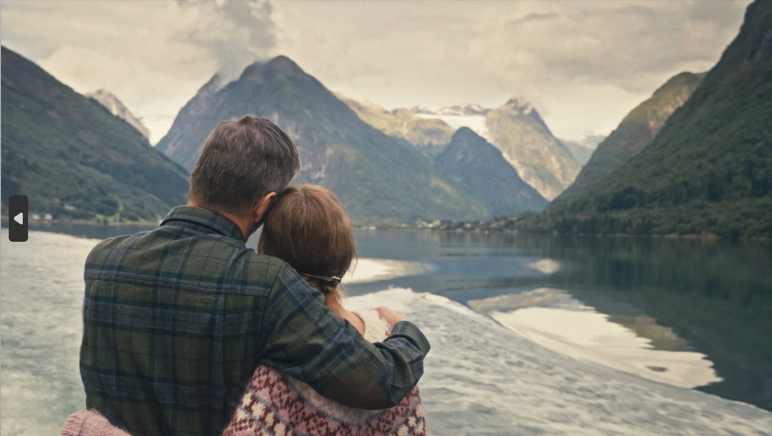 Par klemmer på båt med fjord og snødekte fjell.