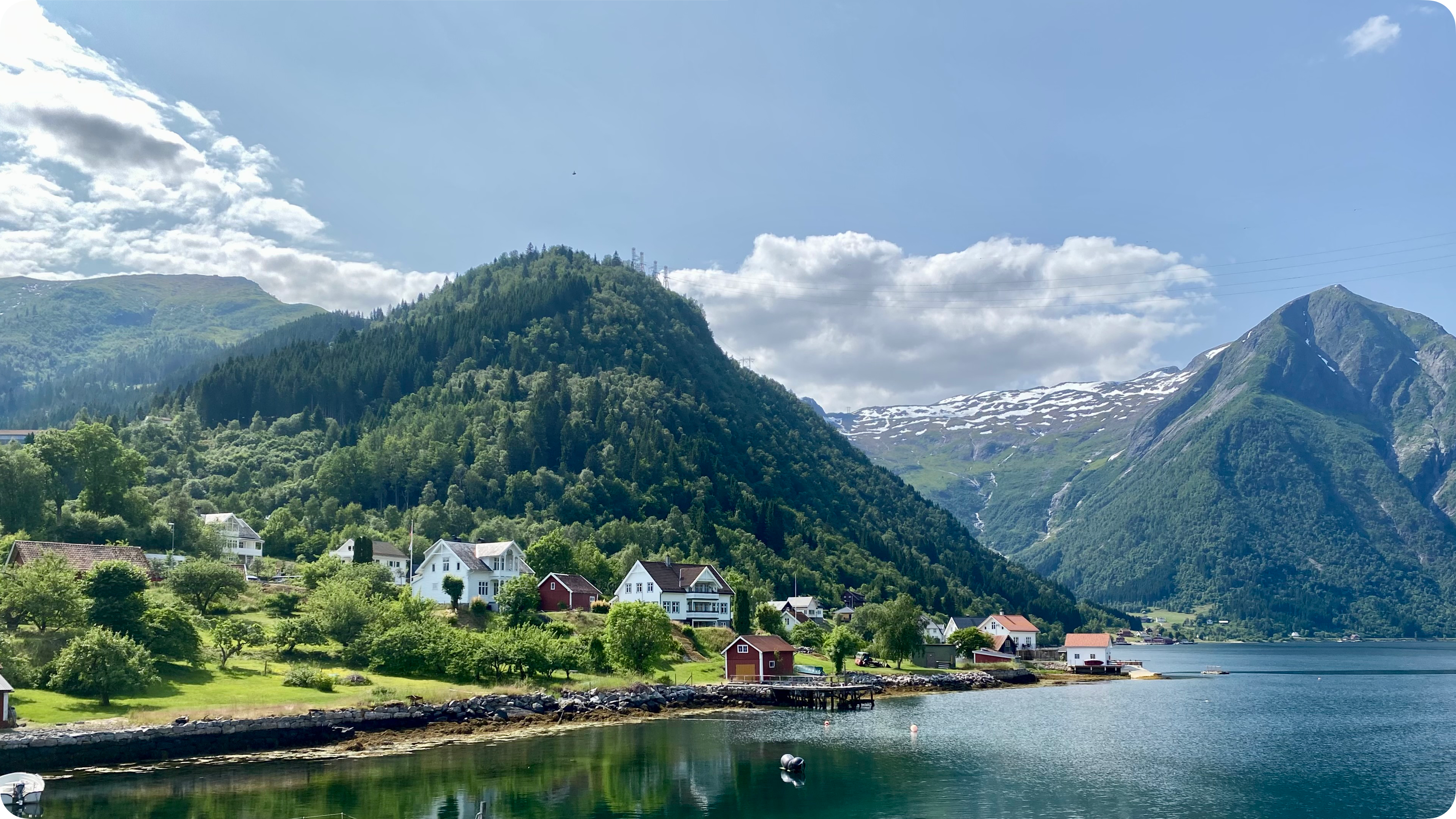 Fjordlandsby med tradisjonelle hus og grønne åser.
