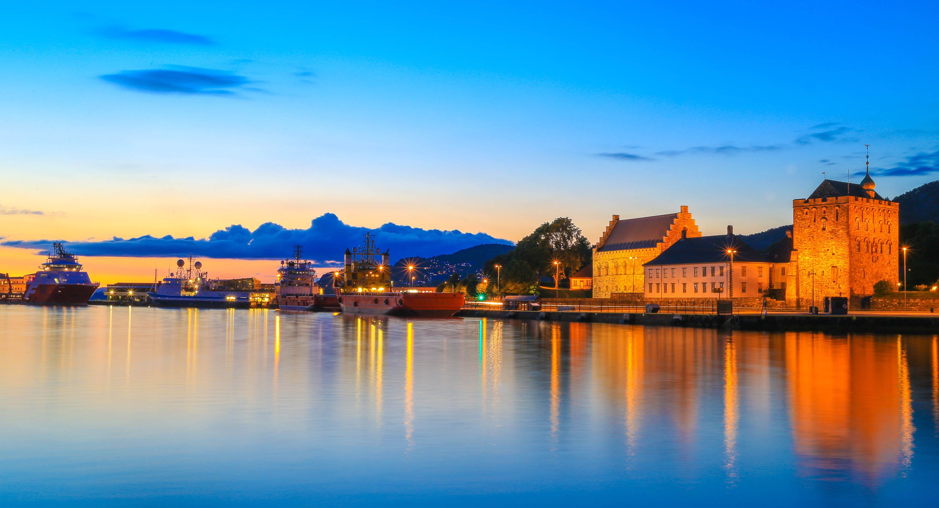 Sunset over Bergen harbor with lit buildings and ship reflections.