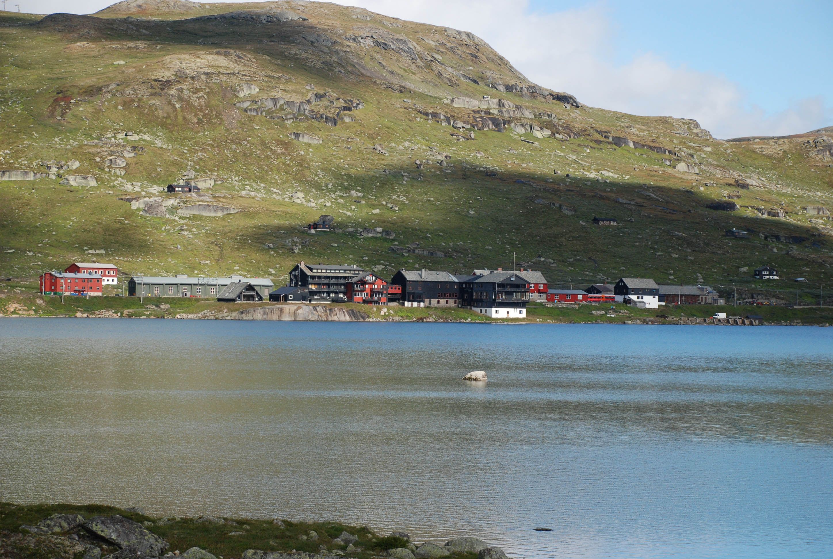 Fargerik fjellandsby ved innsjø med grønne åser.