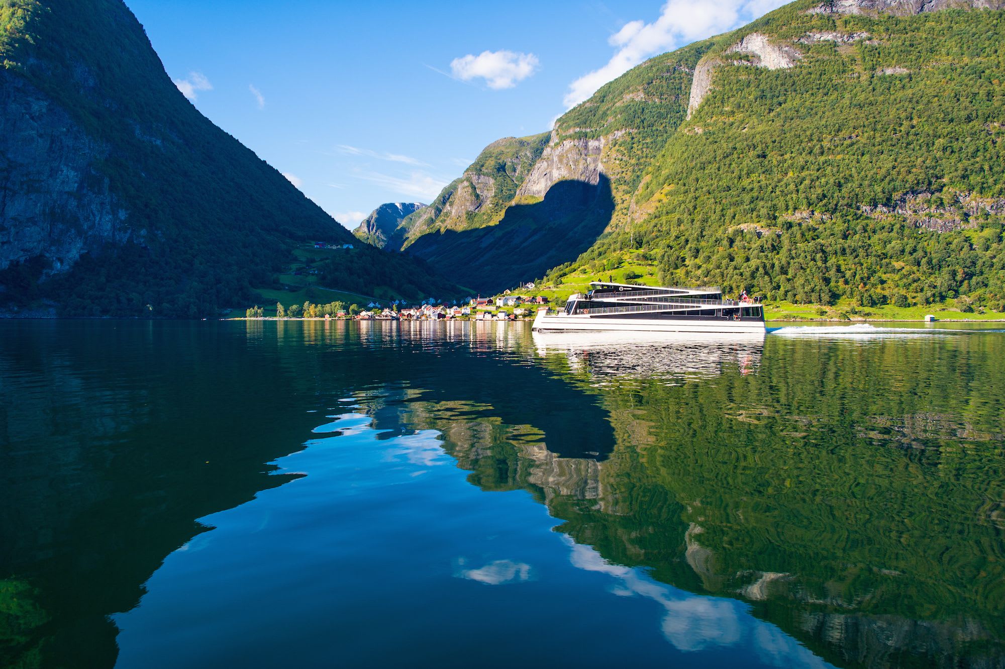 Ferge krysser rolig fjord ved fjell og landsby.