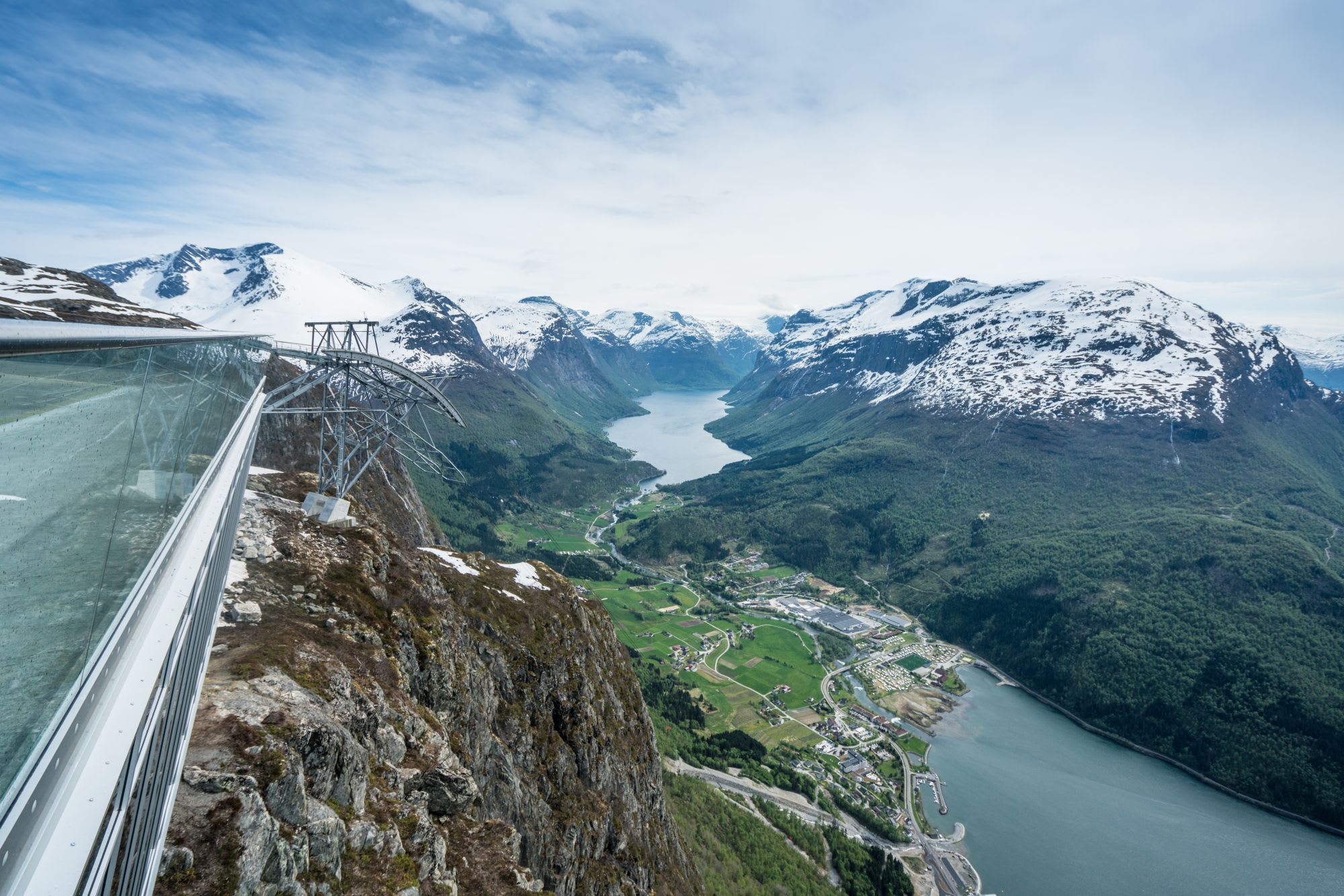 Utsikt fra glassplattform over fjord og snødekte fjell.