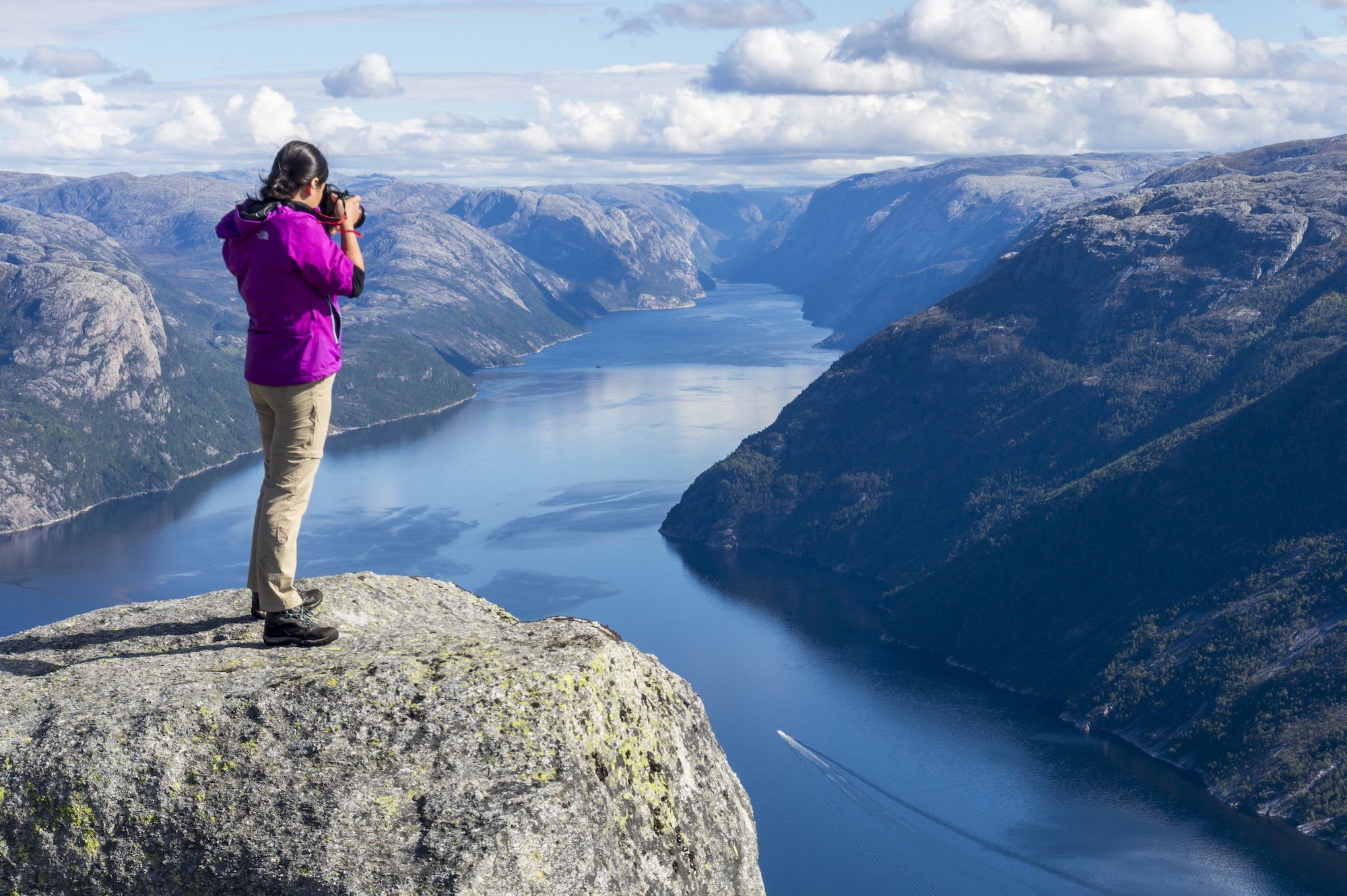 Woman photographs a deep fjord winding through steep mountains.