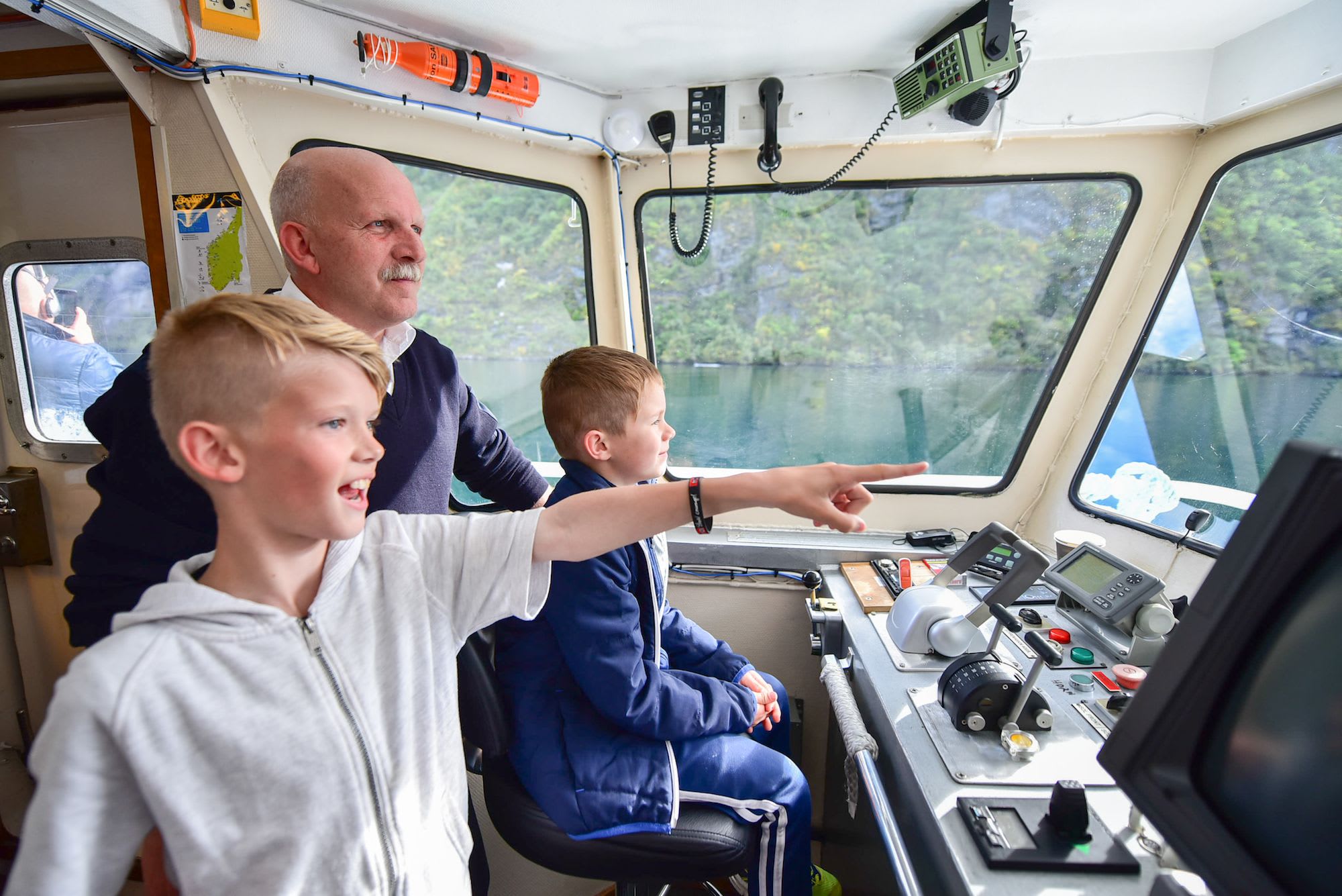 Boys and man in boat control room with views of water and navigation gear.
