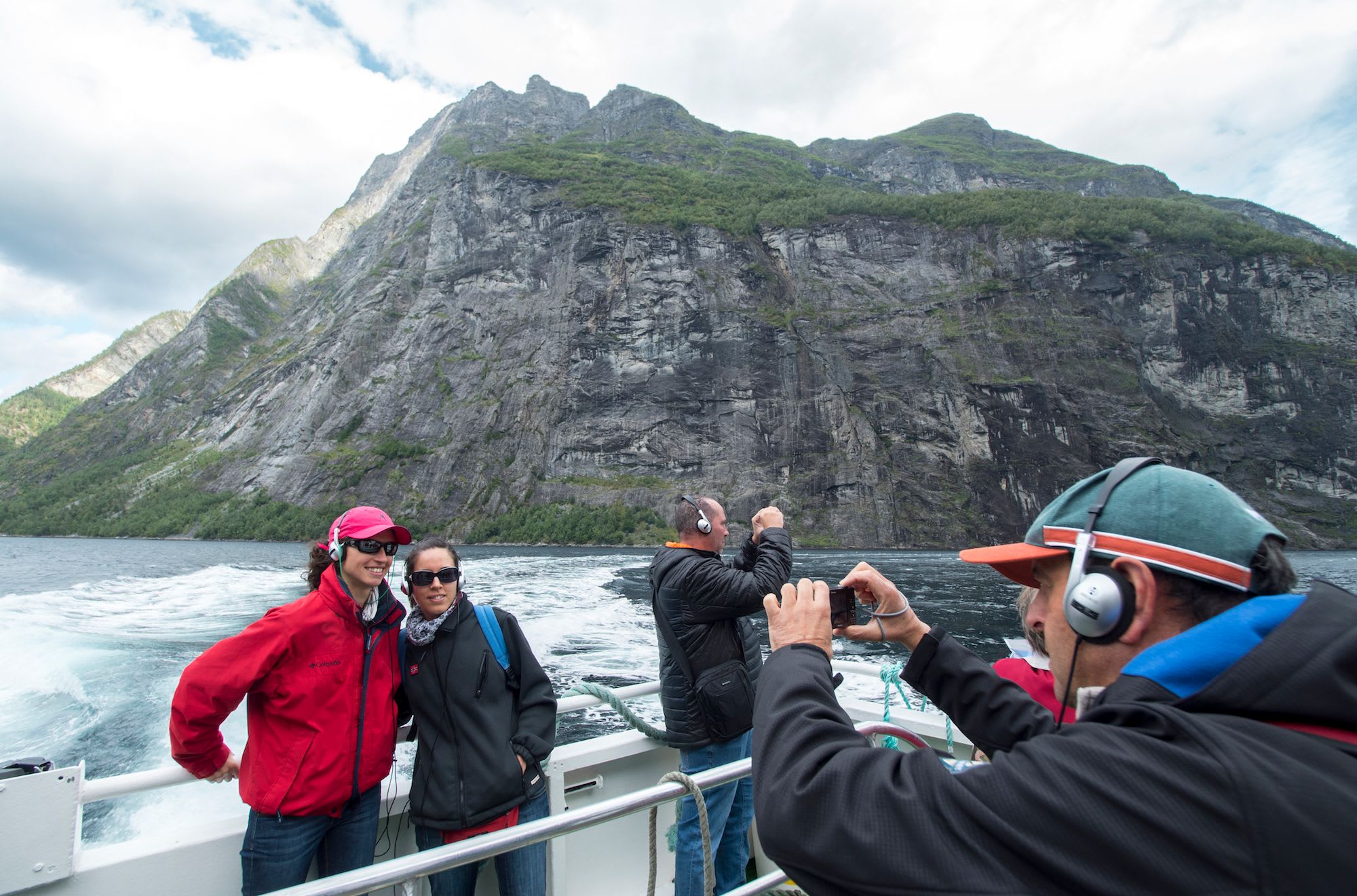 Tourists on the sightseeing tour in the Geirangerfjord take photos of the beautiful fjord landscape.