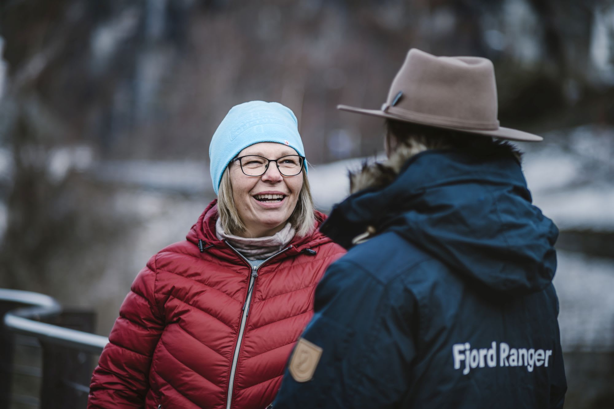 Kvinne i rød boblejakke snakker med Fjord Ranger på vintercruise på Geirangerfjorden.