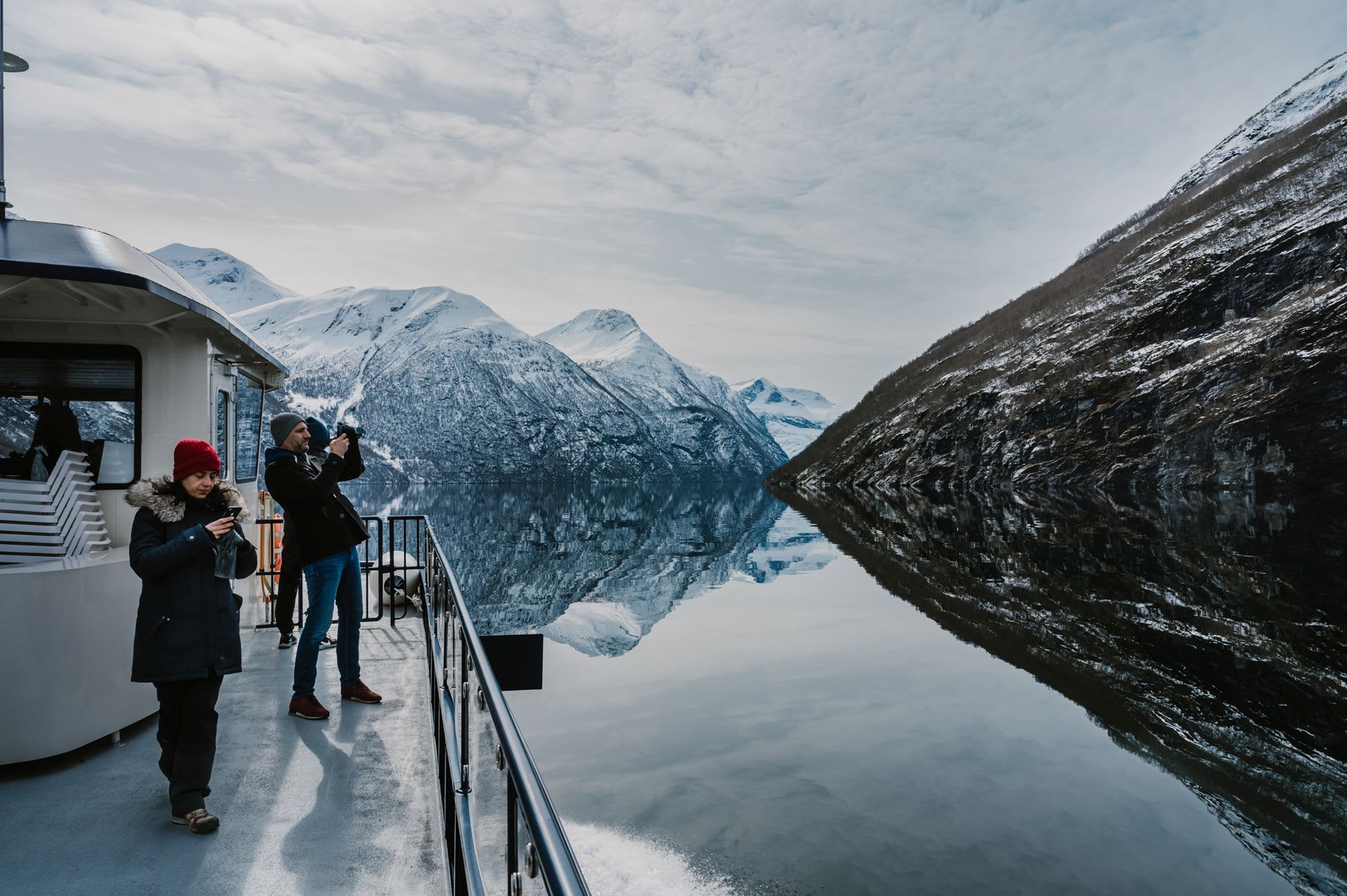 Tourists on the boat deck on the winter cruise on the Geirangerfjord surrounded by a beautiful world heritage landscape