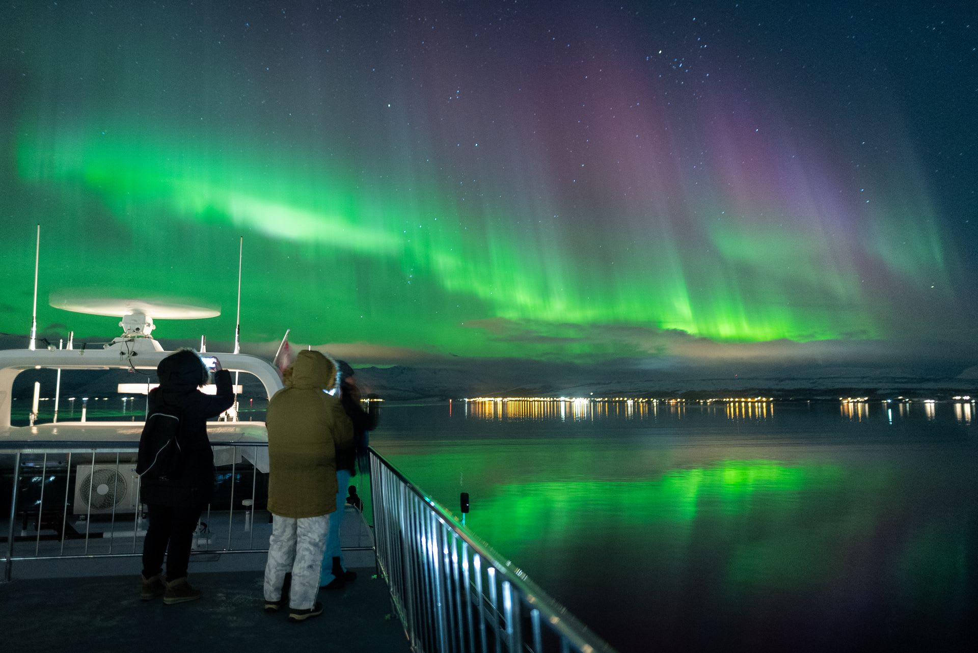 Menschen auf der Nordlichtkreuzfahrt in Tromsø machen Fotos von den über ihnen tanzenden Nordlichtern.