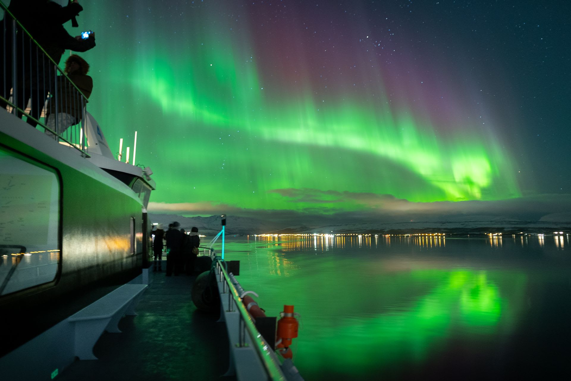 Menschen auf einem Boot fotografieren das Nordlicht, das den arktischen Himmel erleuchtet in Tromsø.