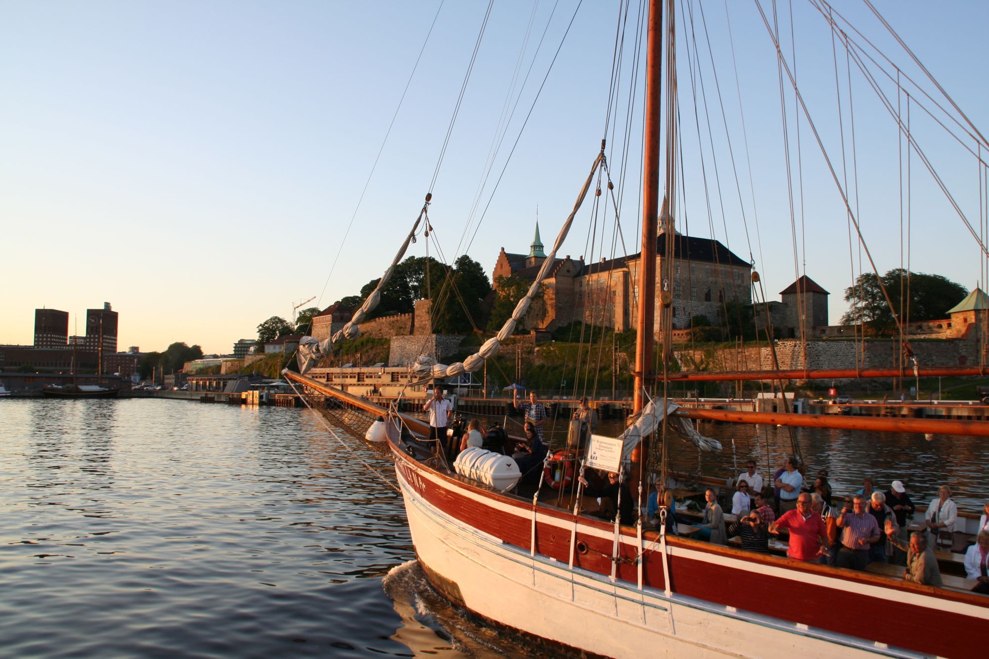 Tourists on fjord cruise on the Oslofjord pass historic Akershus fortress at sunset.