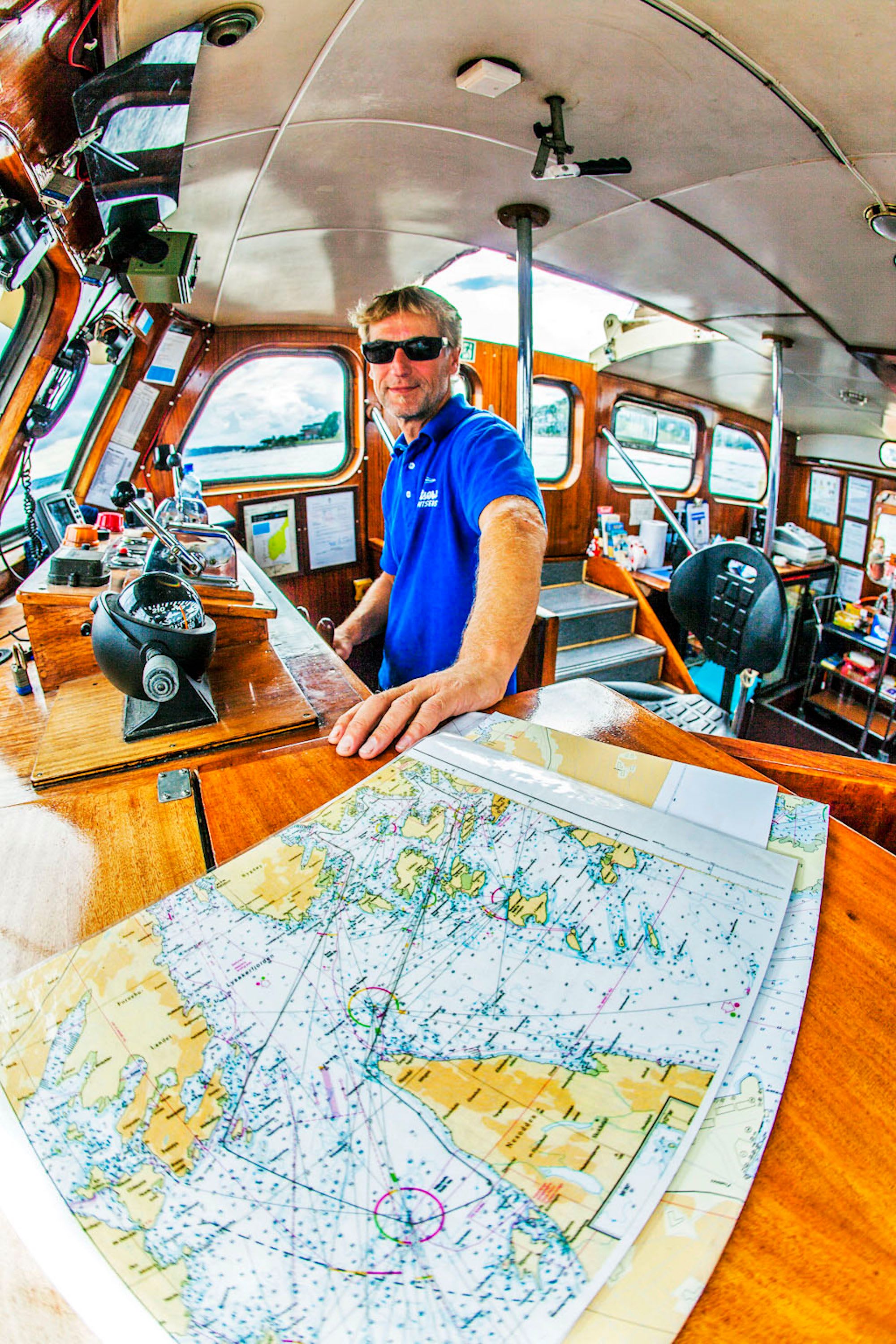 Boat captain in sunglasses at the helm with chart in foreground.