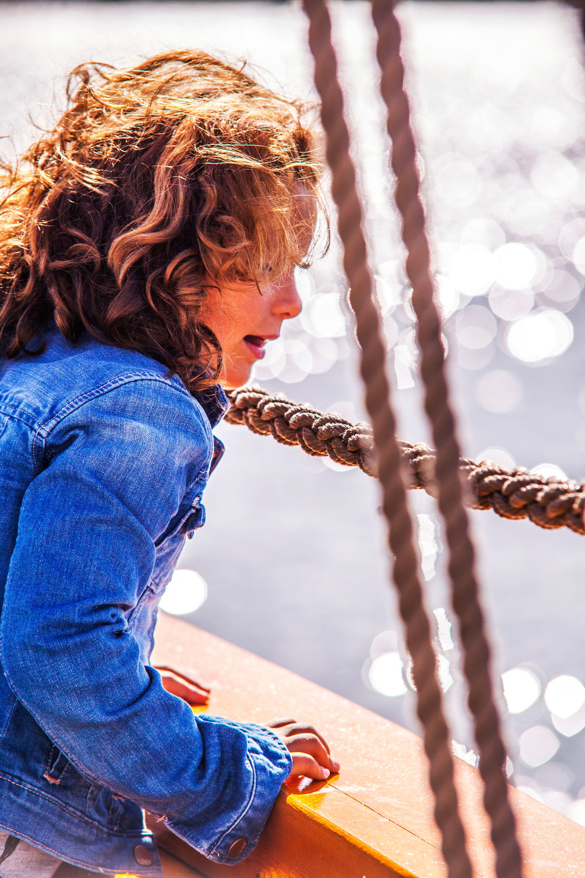 Child in denim leans over boat rail as sun sparkles on the Oslofjord.