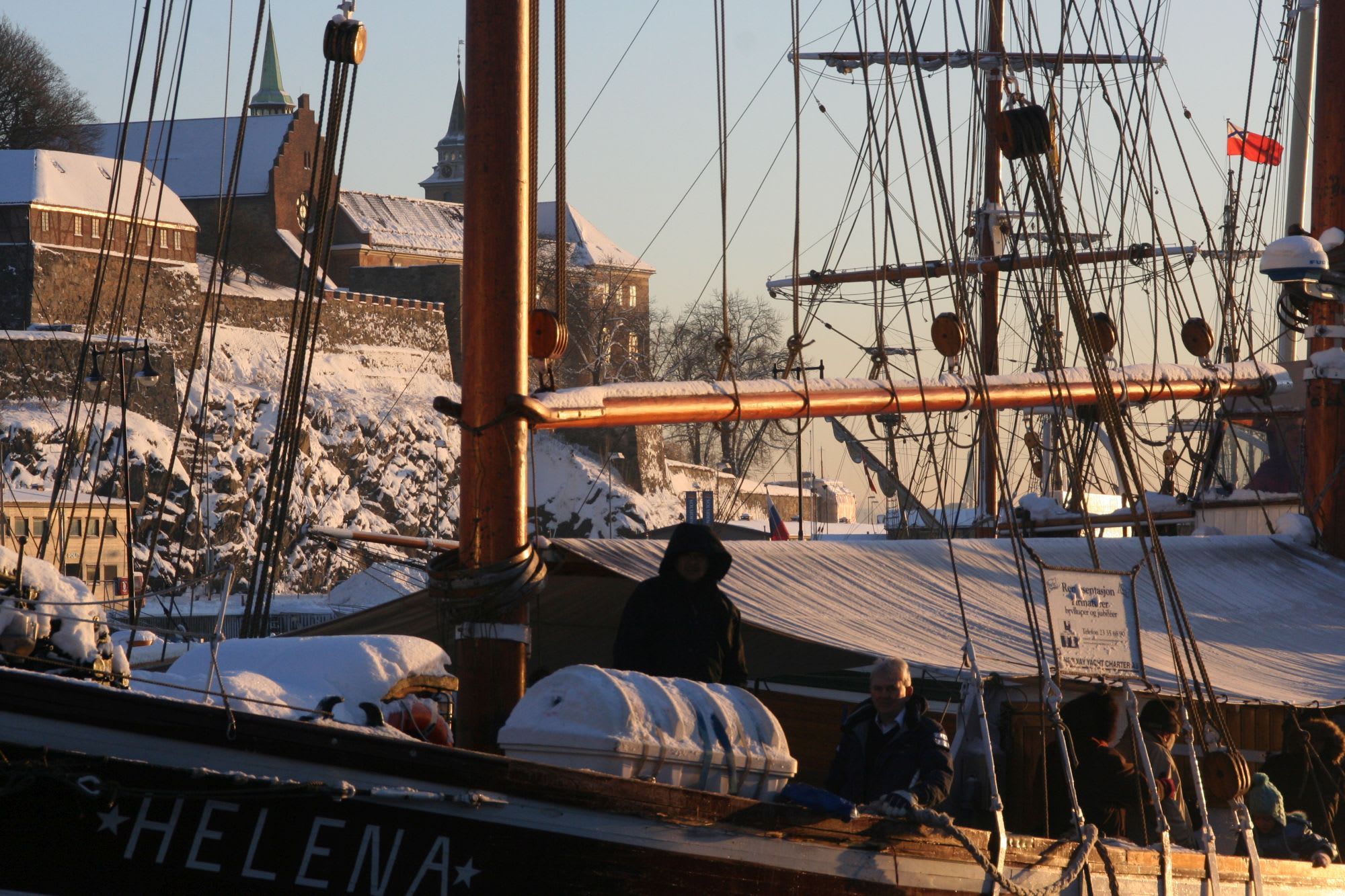 Wooden sailboat "HELENA" docked in the snowy harbor in Oslo me d Akershus Fortress in the back ground.