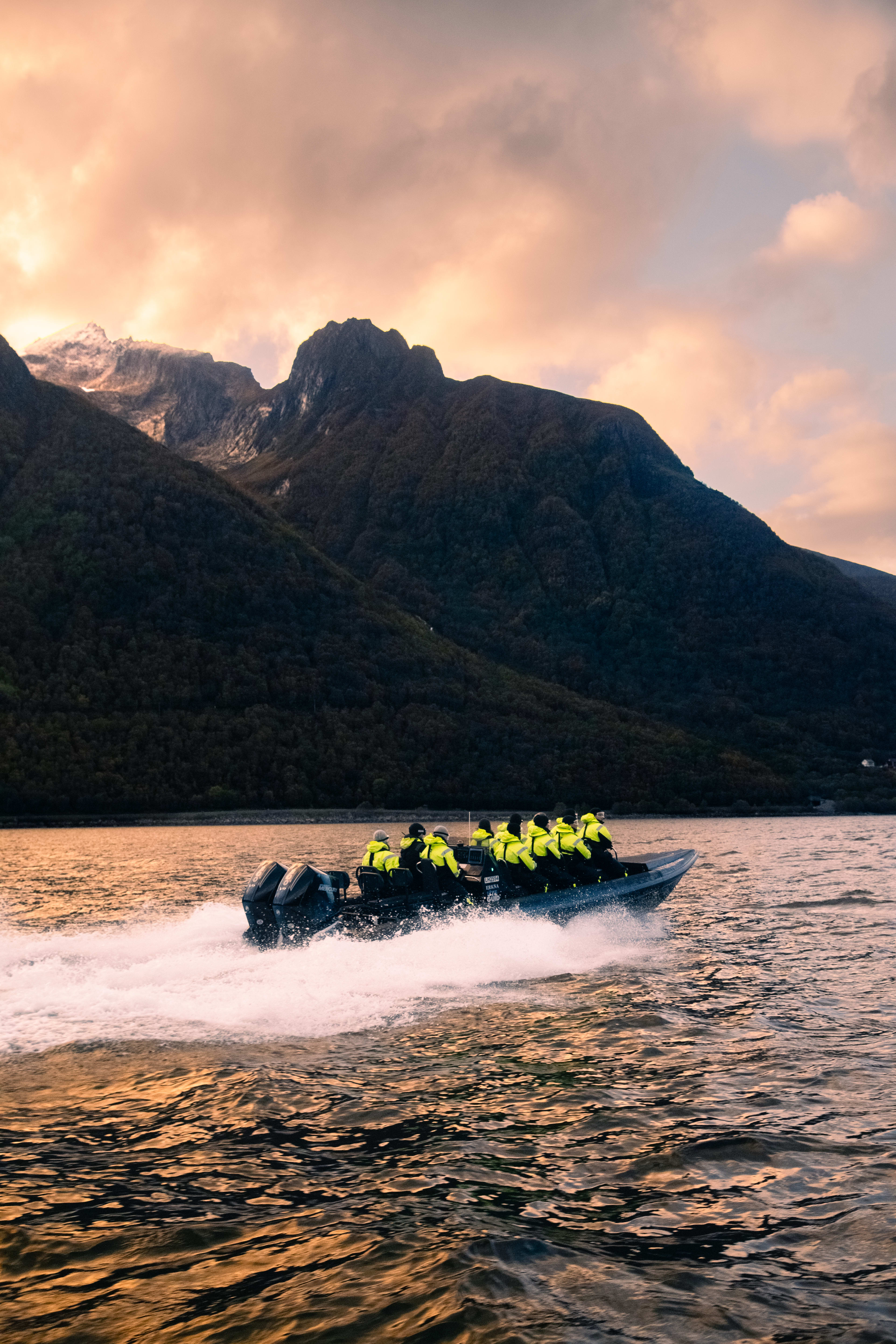 RIB-båt på vei til Hjørundfjorden fra Ålesund ved solnedgang med fjelltopper og bølger i norsk fjordlandskap på Sunnmøre