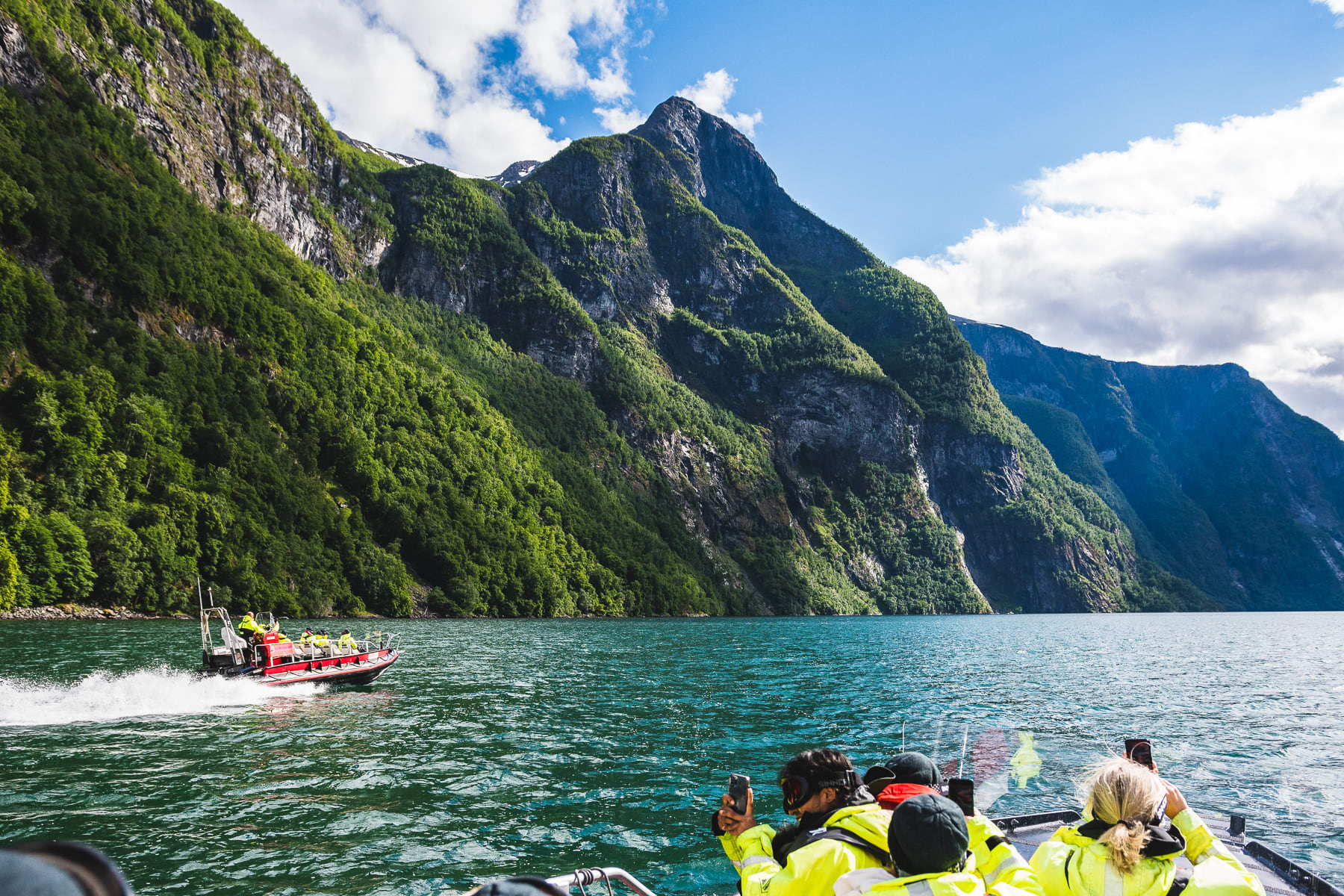 Fjord safari boats sailing on Nærøyfjord toward Sagofossen waterfall near Flåm on a sunny summer day