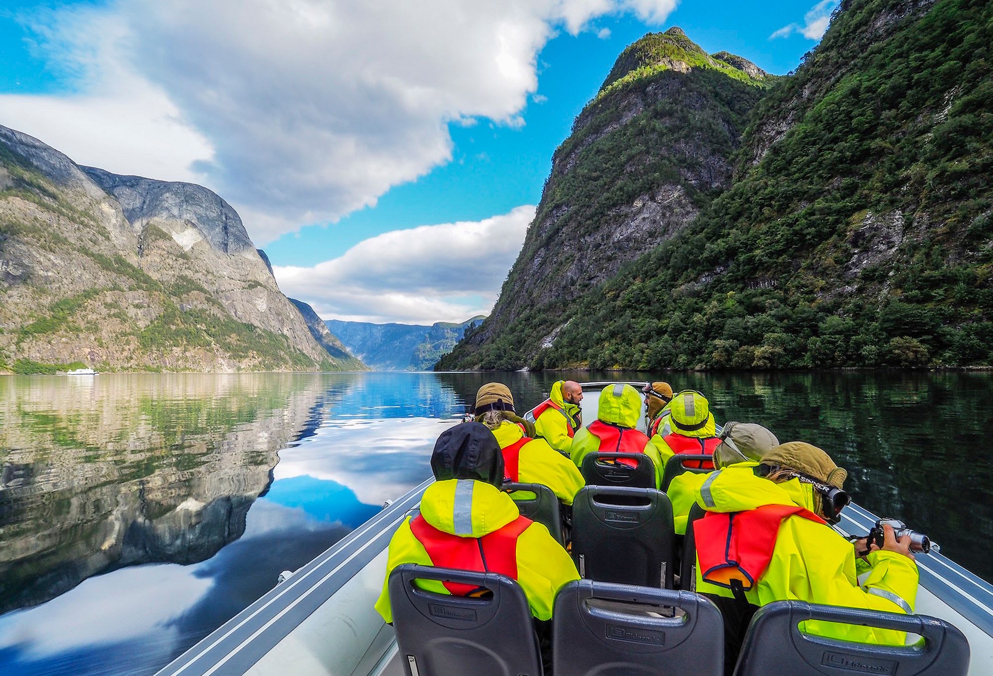People on a Rib boat safari in the beautiful Nærøyfjord with mirrored cliffs and cloudy skies.