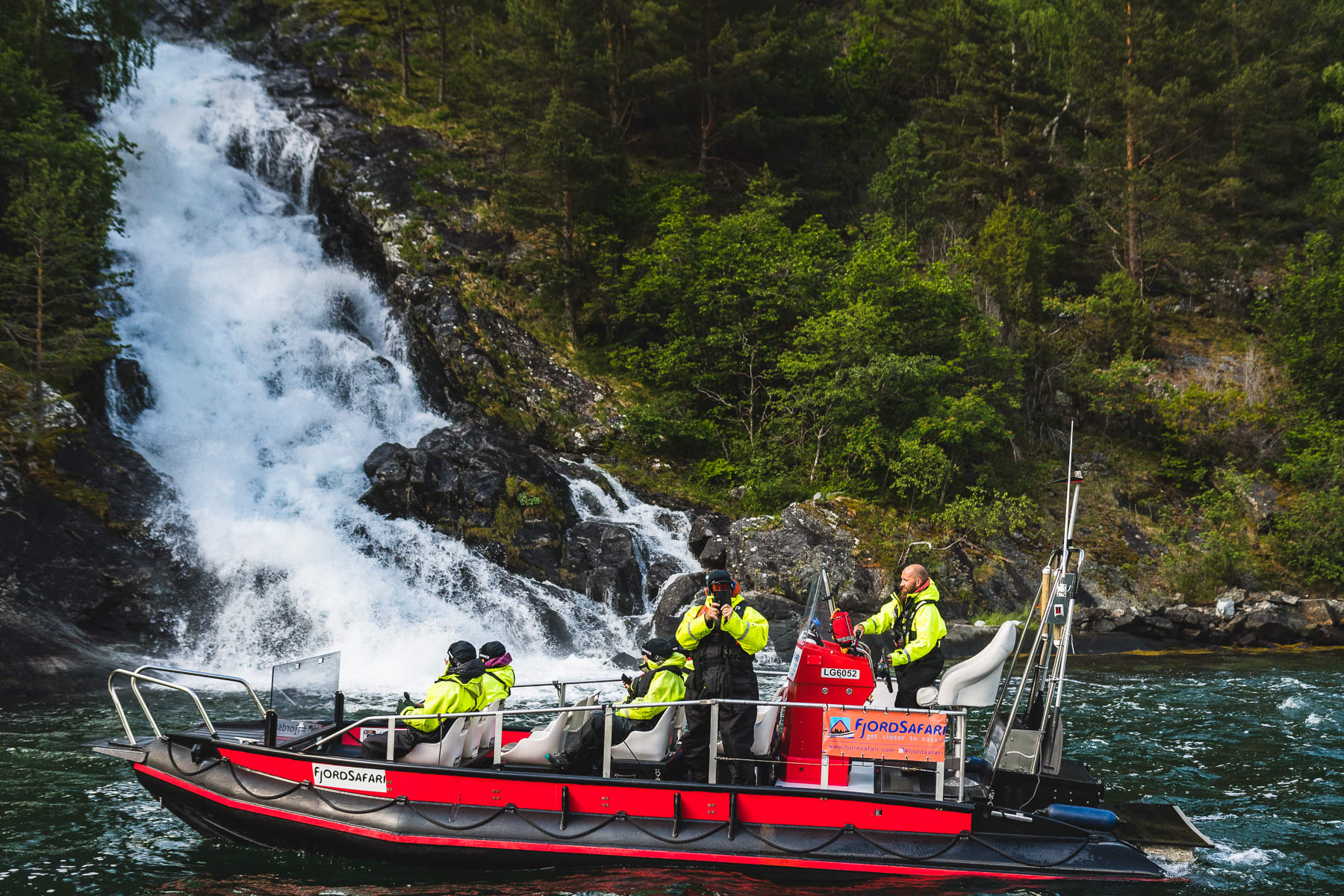 Fjord safari boat approaching Sagofossen waterfall in Flåm - guests feeling the waterfall mist
