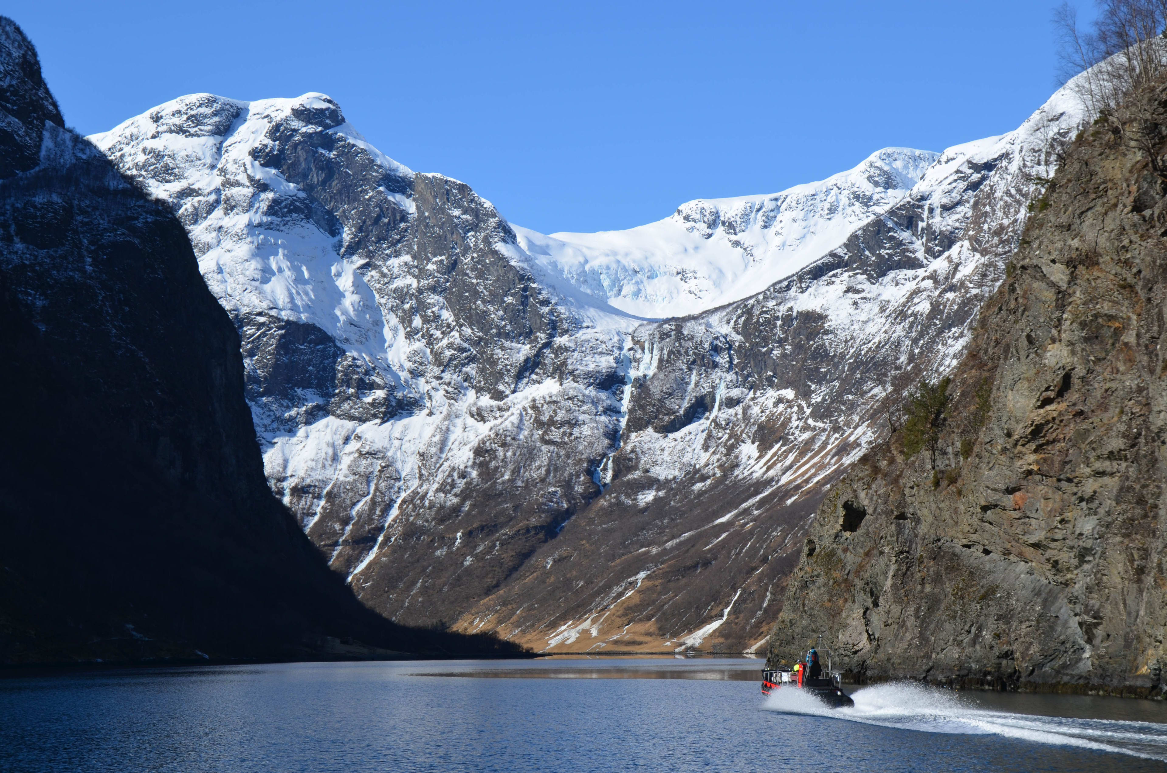 Båten suser gjennom Nærøyfjorden fra Flåm, omgitt av snødekte fjelltopper.