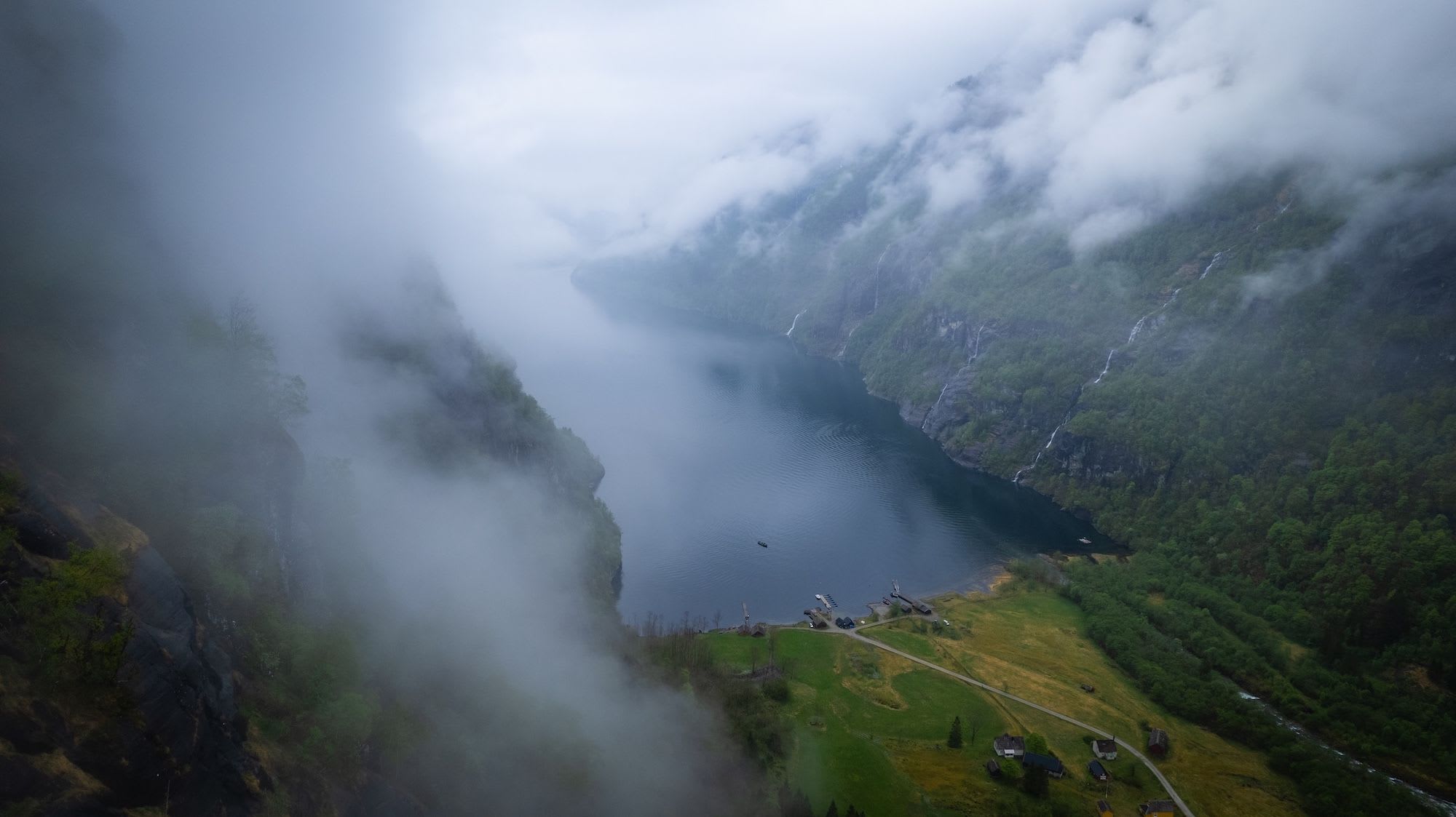 Aerial view of a misty Hardangerfjord with waterfalls and houses.