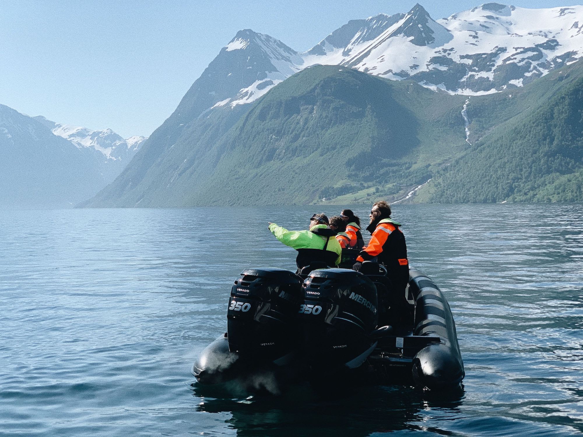 RIB boat floats on fjord, passengers admire view.
