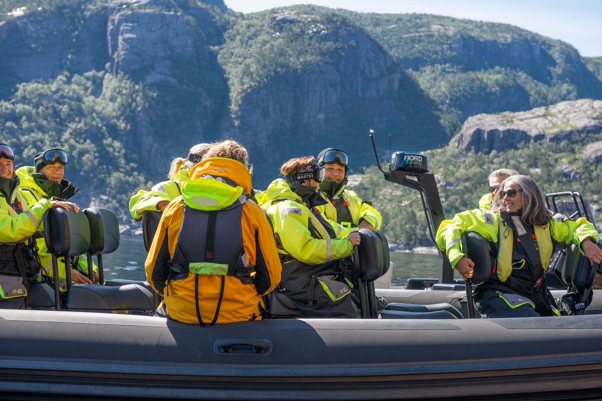A group of passengers in neon green jackets enjoying a fjord tour, seated in a black inflatable speedboat.