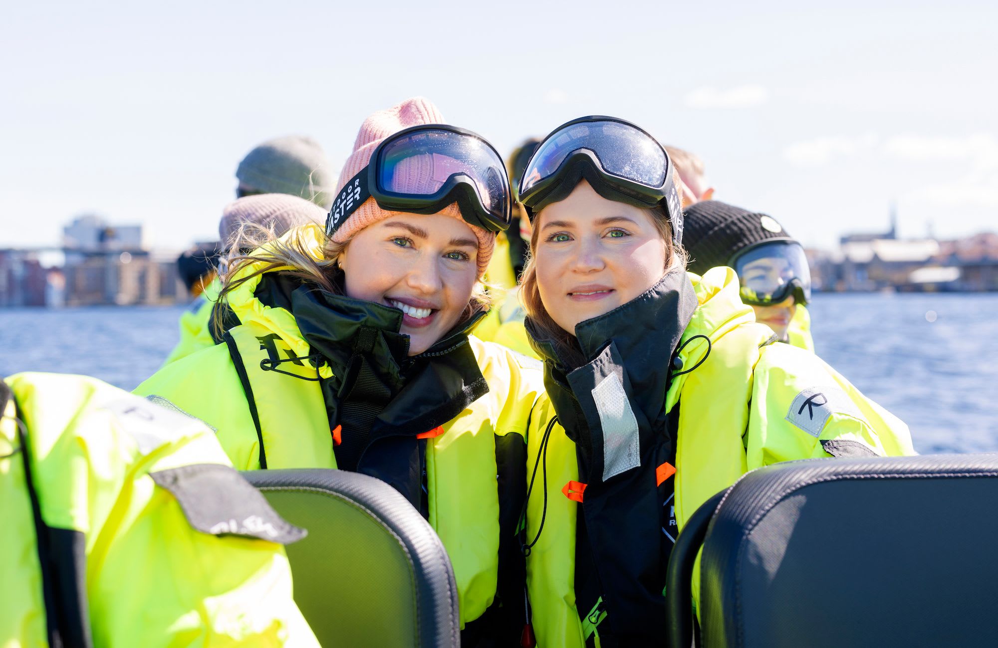 Two smiling women in neon green jackets, sitting closely on a RIB boat tour on Lysefjord.