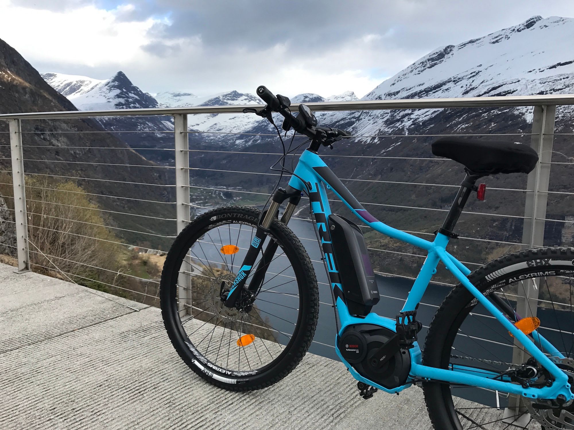 Blå elsykkel på utsiktspunkt med fjord og snødekte fjell.