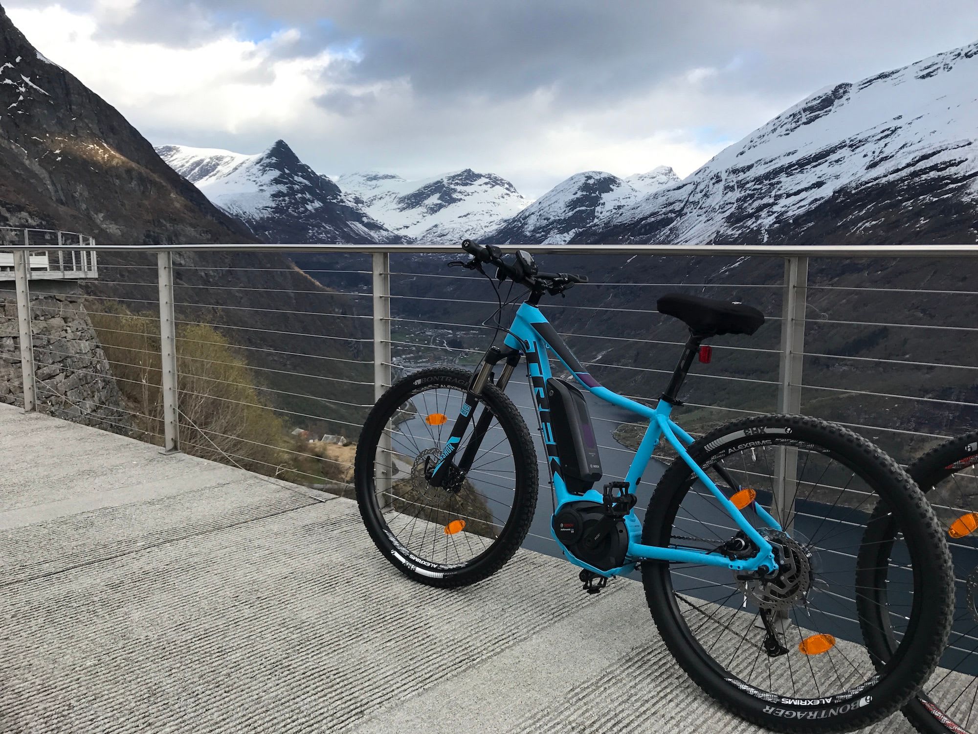 Blå elsykkel på utsiktsplattform med snødekte fjorder.